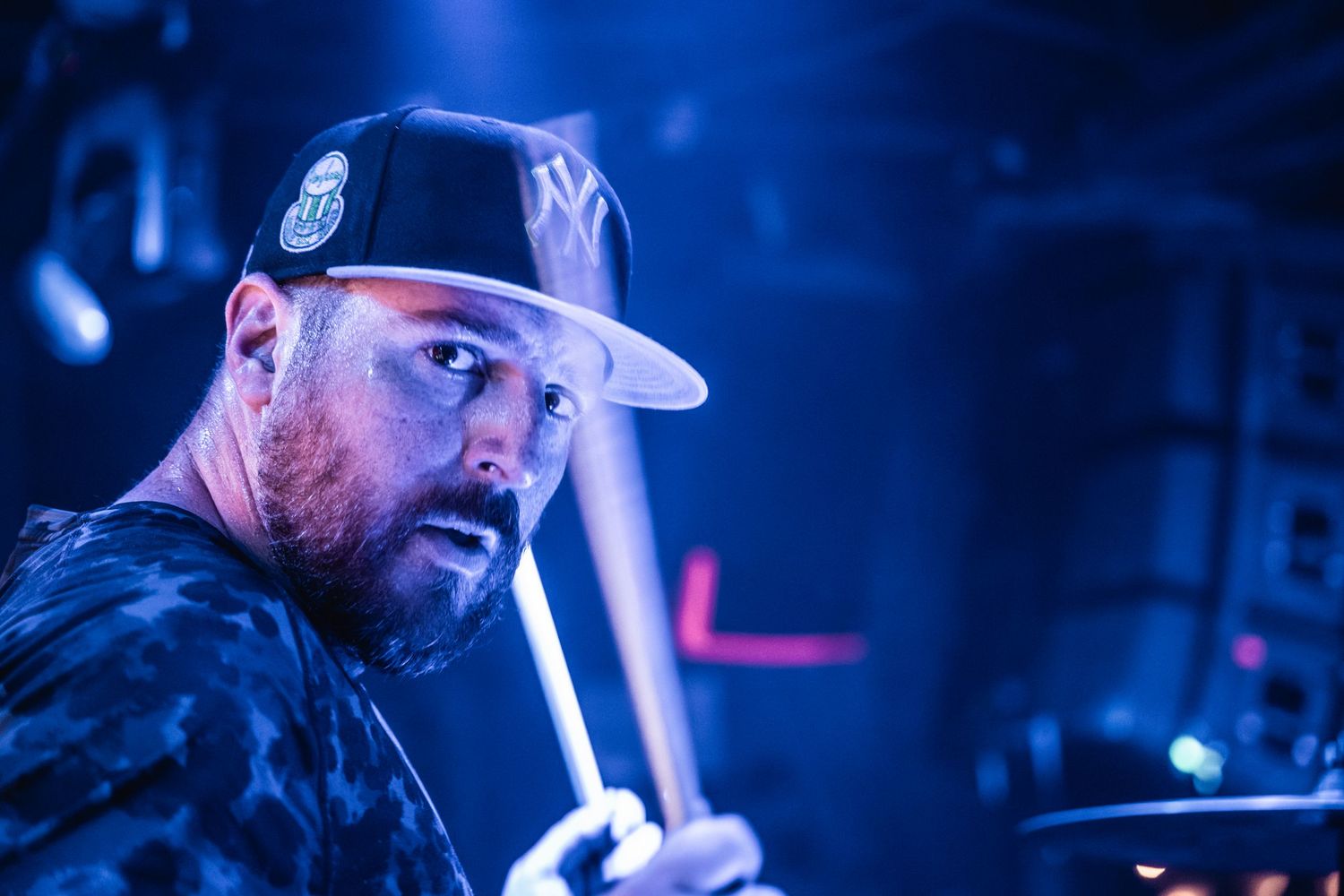 Concert performer in a baseball cap illuminated by blue stage lighting during a live music performance.