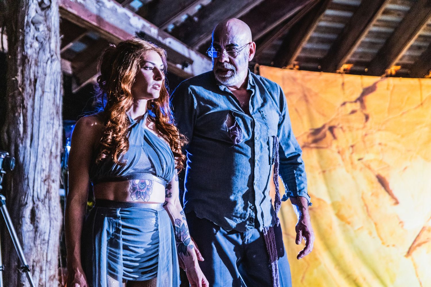 A couple in denim outfits dance together in a rustic wooden barn setting with warm lighting.