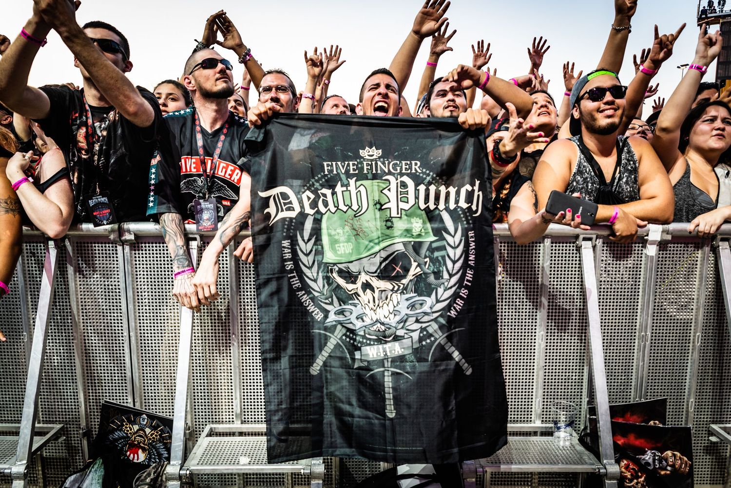 An energetic crowd of fans cheering behind metal barriers at what appears to be a concert or festival event.