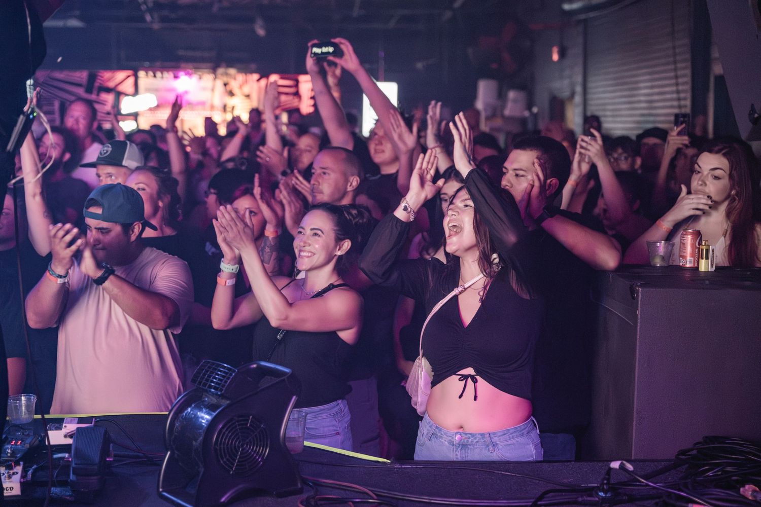 Crowd of people dancing and enjoying themselves at a nightclub with colorful lighting and vibrant atmosphere.