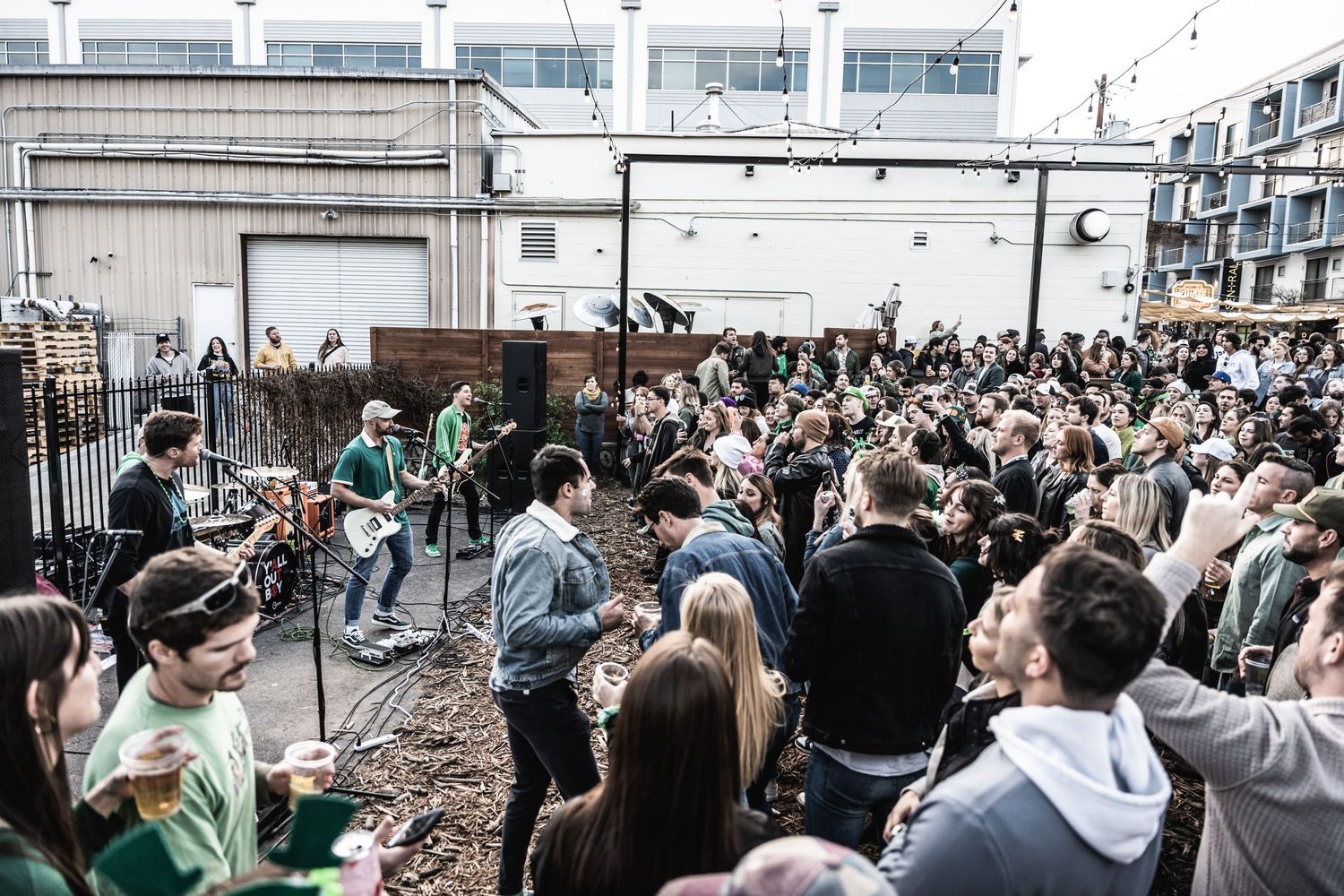 Live band performing to packed crowd at outdoor music venue.