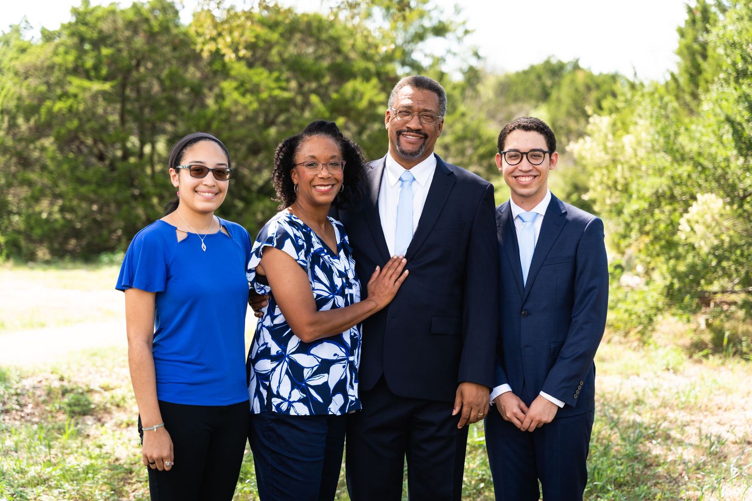 Group of four professionals in business attire standing together outdoors on a sunny day.