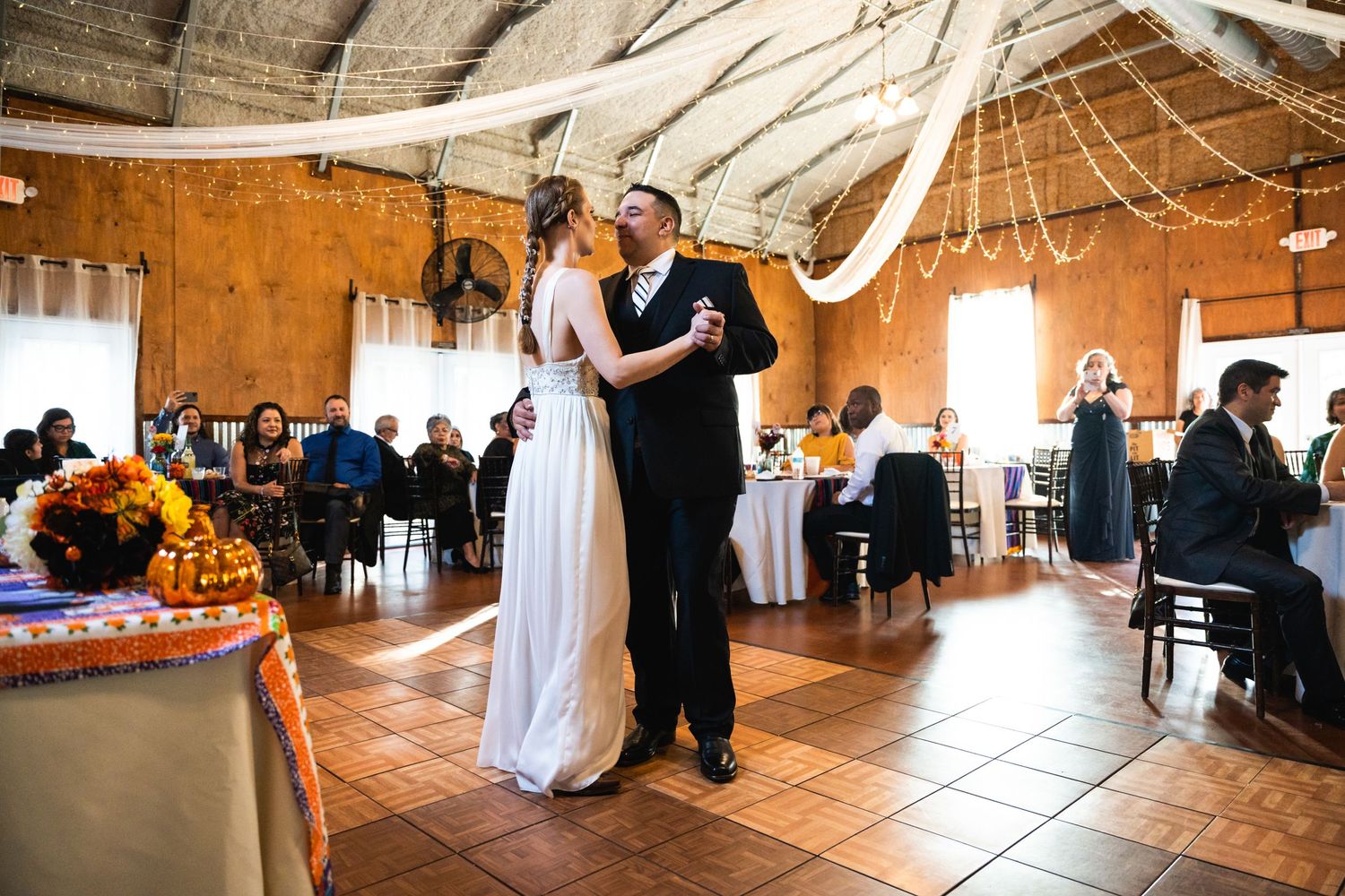 Newlyweds dancing together in a rustic barn venue decorated with white draping and string lights.