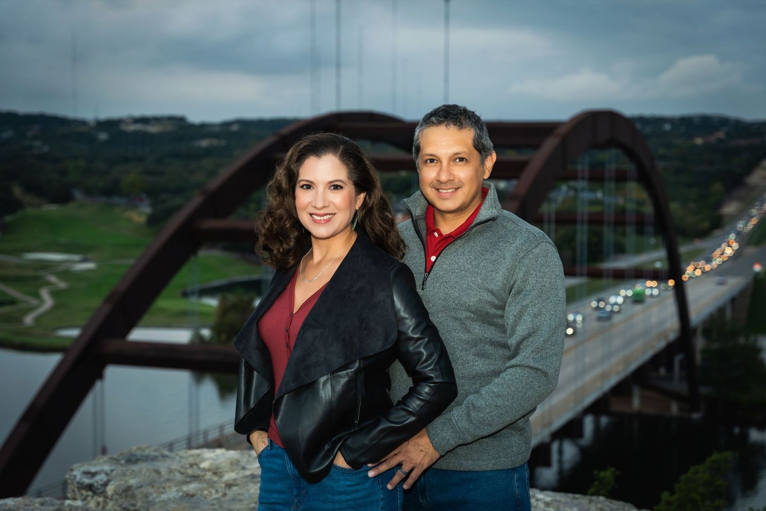 Couple poses together with Pennybacker Bridge and scenic Austin landscape in background.