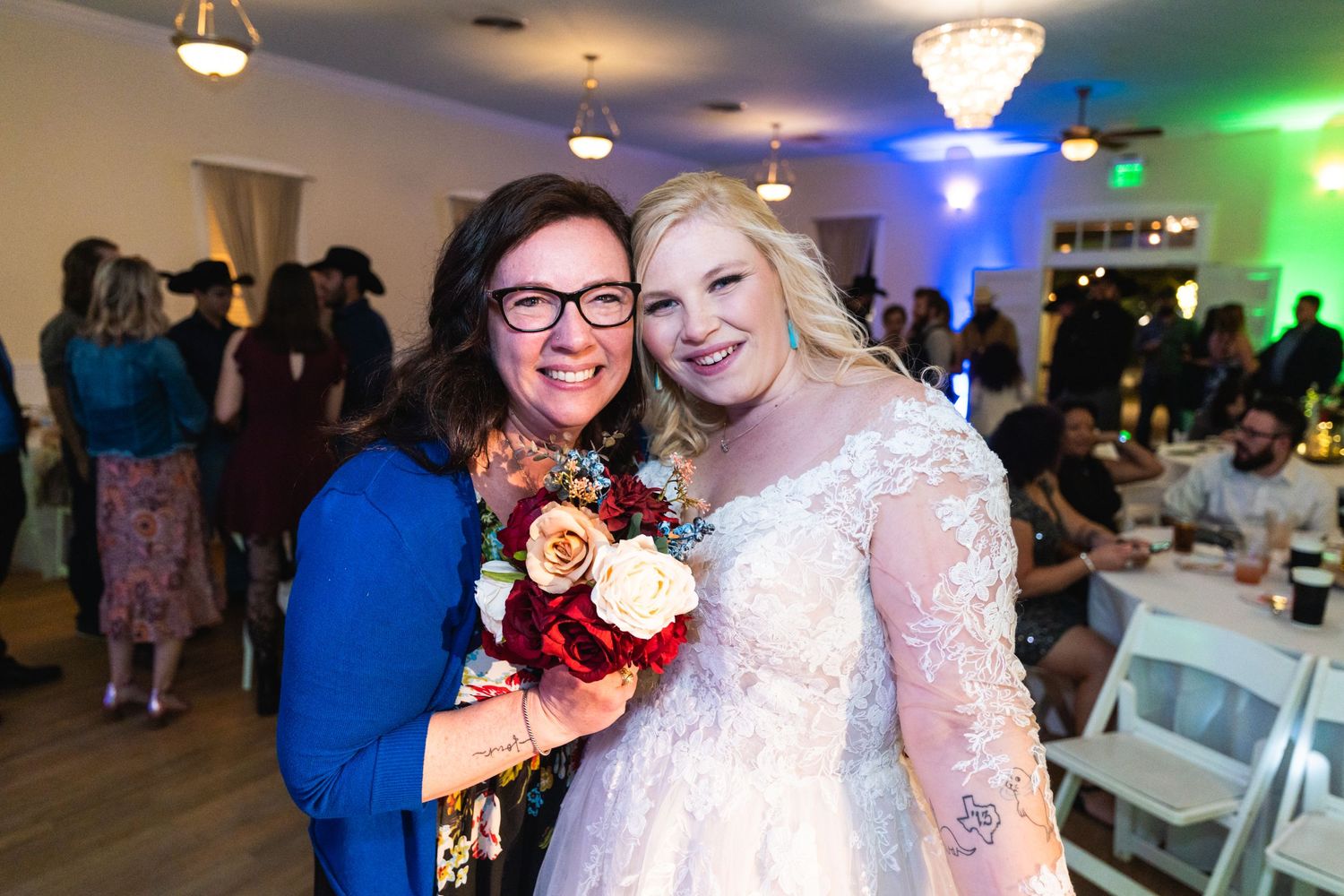 Two people pose with a burgundy and white bouquet at a wedding reception.