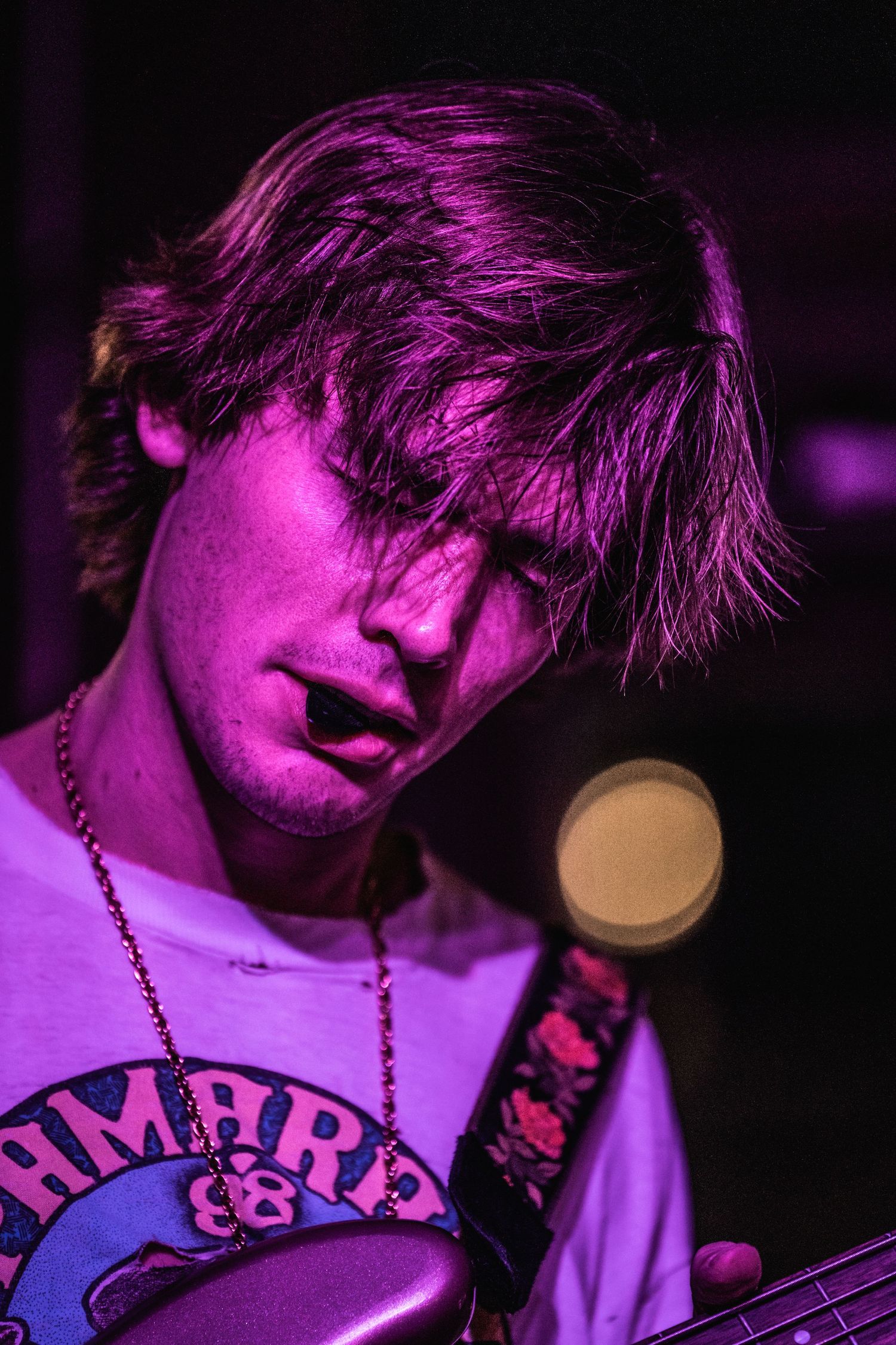Musician performing on stage bathed in vibrant purple lighting while holding a guitar.