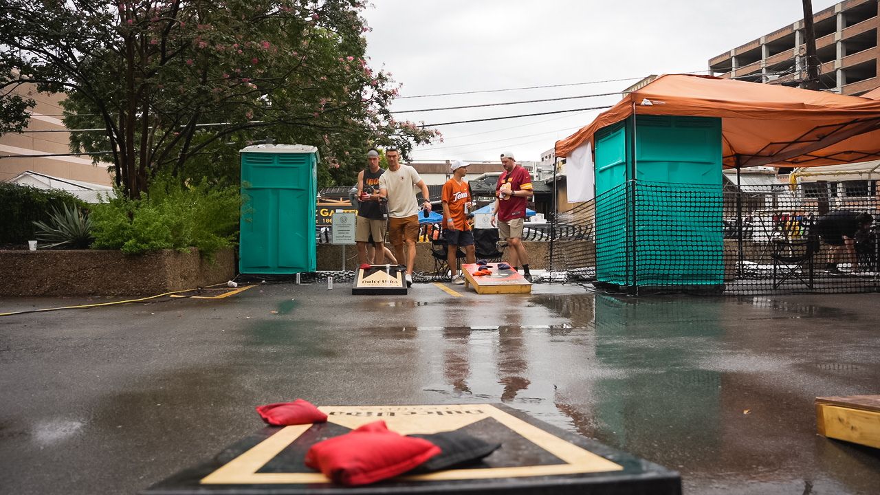 Portable restrooms set up on wet pavement at outdoor event with attendees in background.