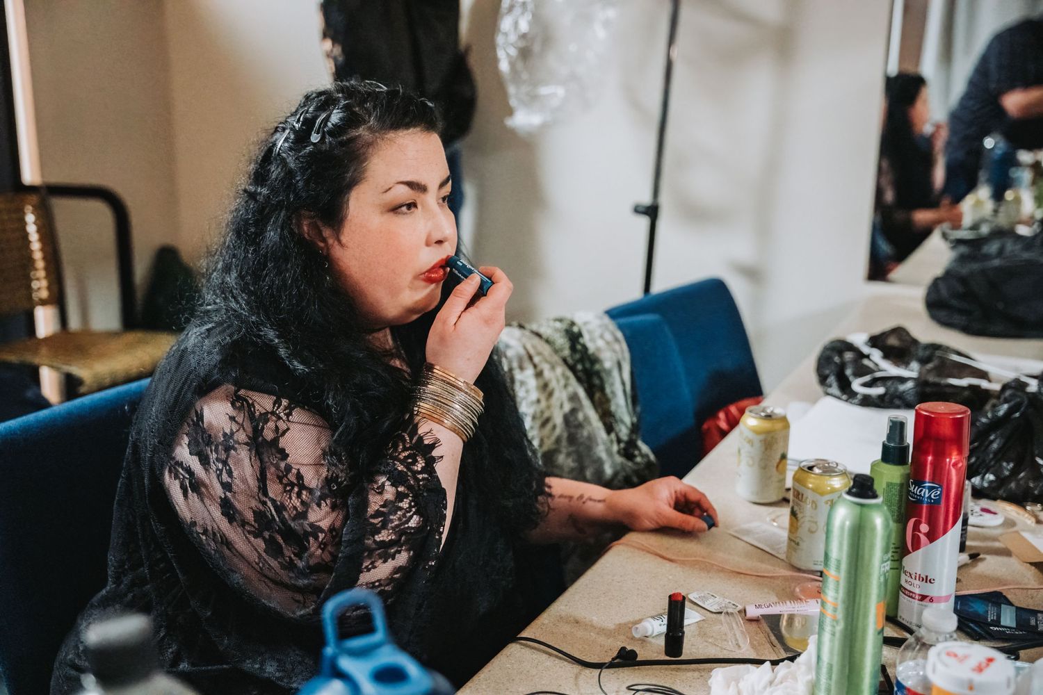 Person in black lace preparing makeup in a backstage dressing room.