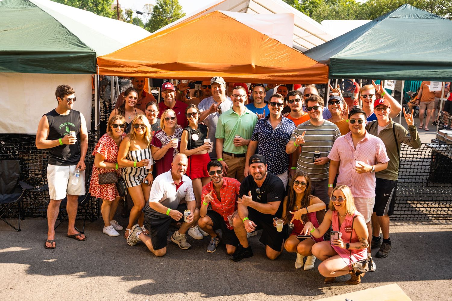 Large group of college sports fans pose together under canopy tents at an outdoor event.