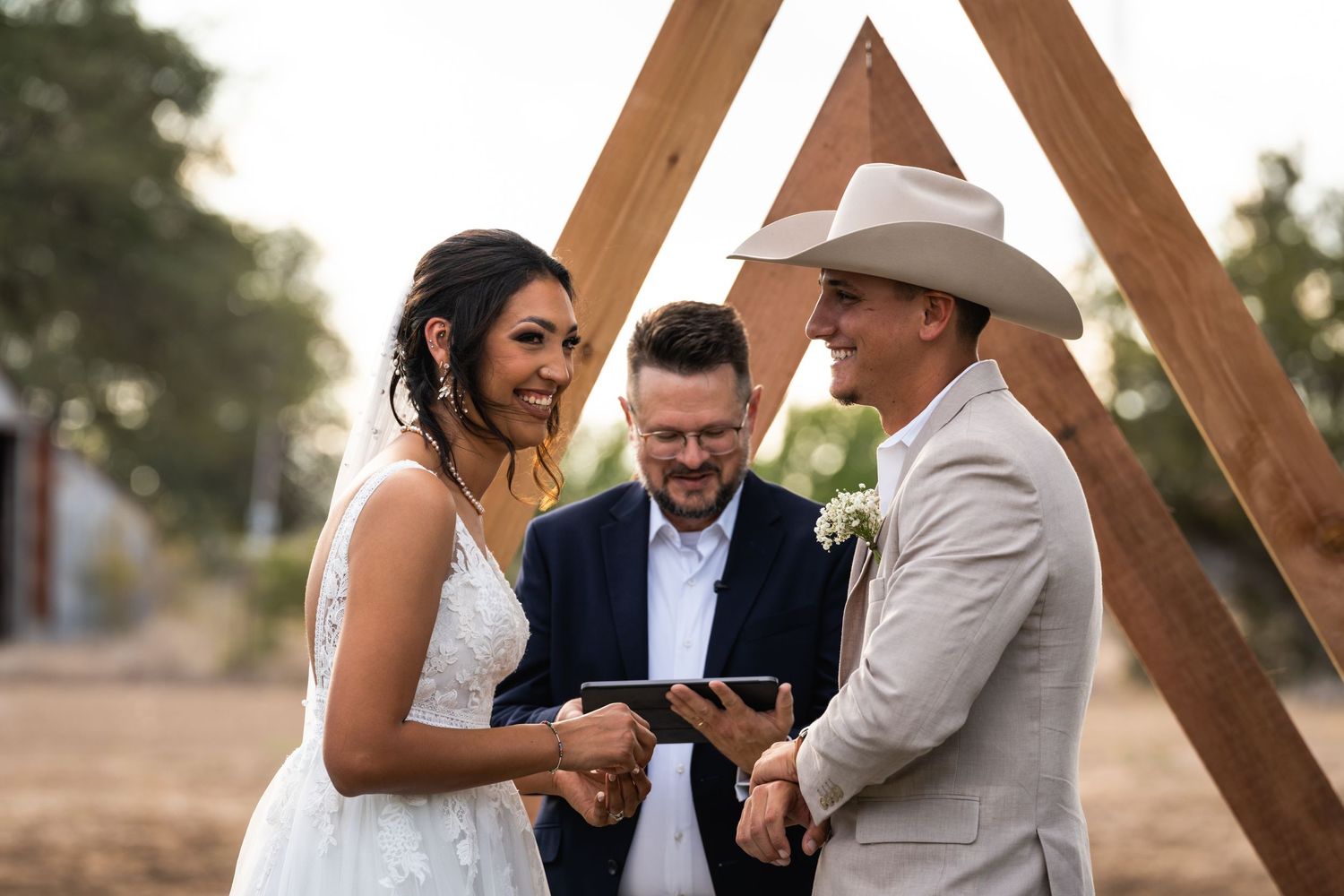 A wedding ceremony takes place under a rustic wooden triangle arch.