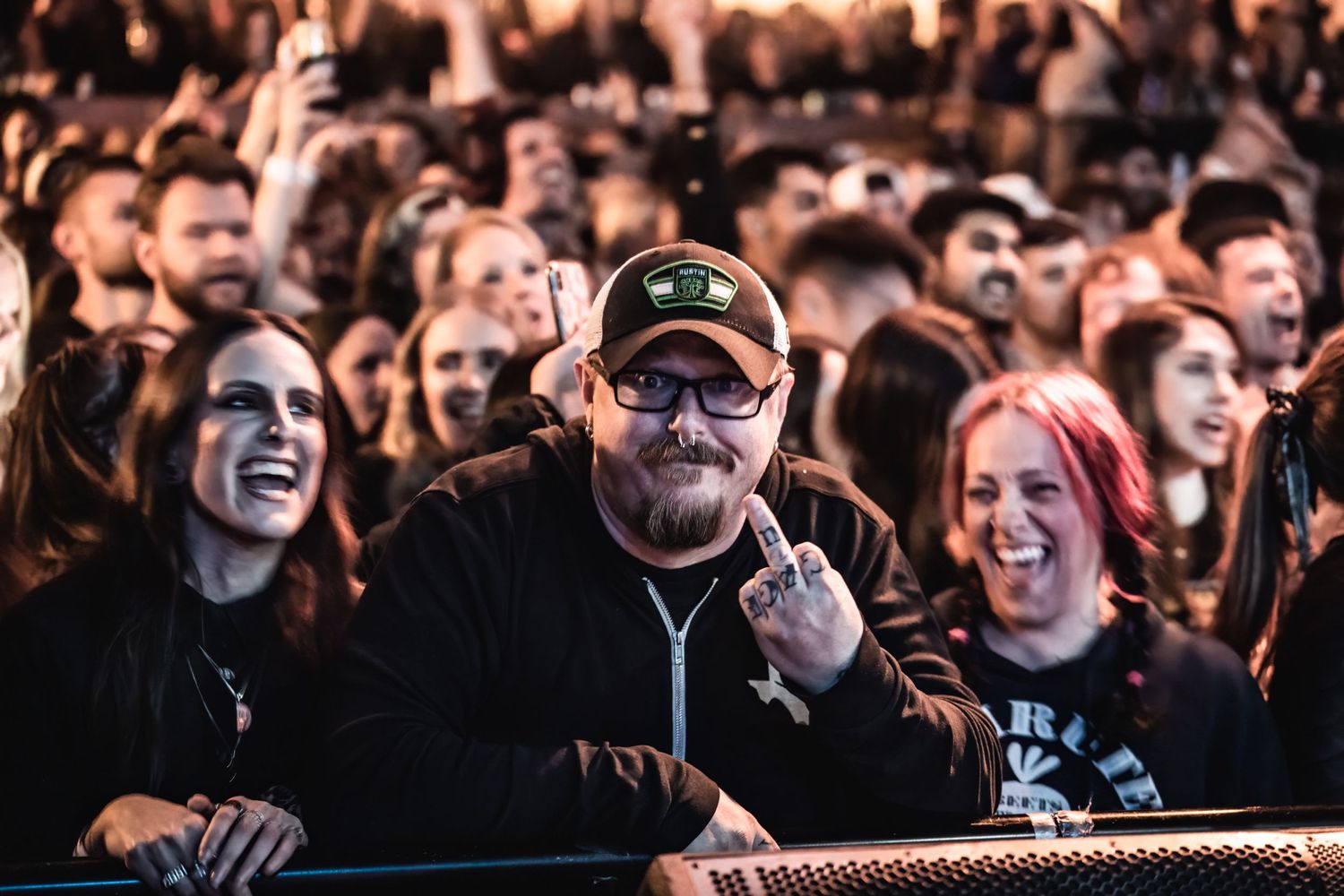 Excited concert audience members smile and gesture at barrier during live music show.