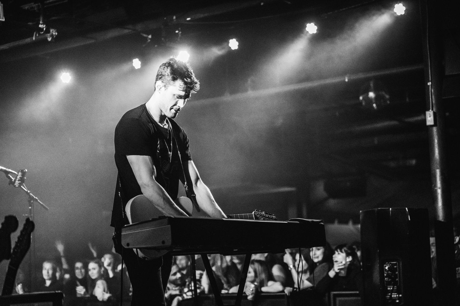 Musician performing on keyboard during live concert with dramatic stage lighting.