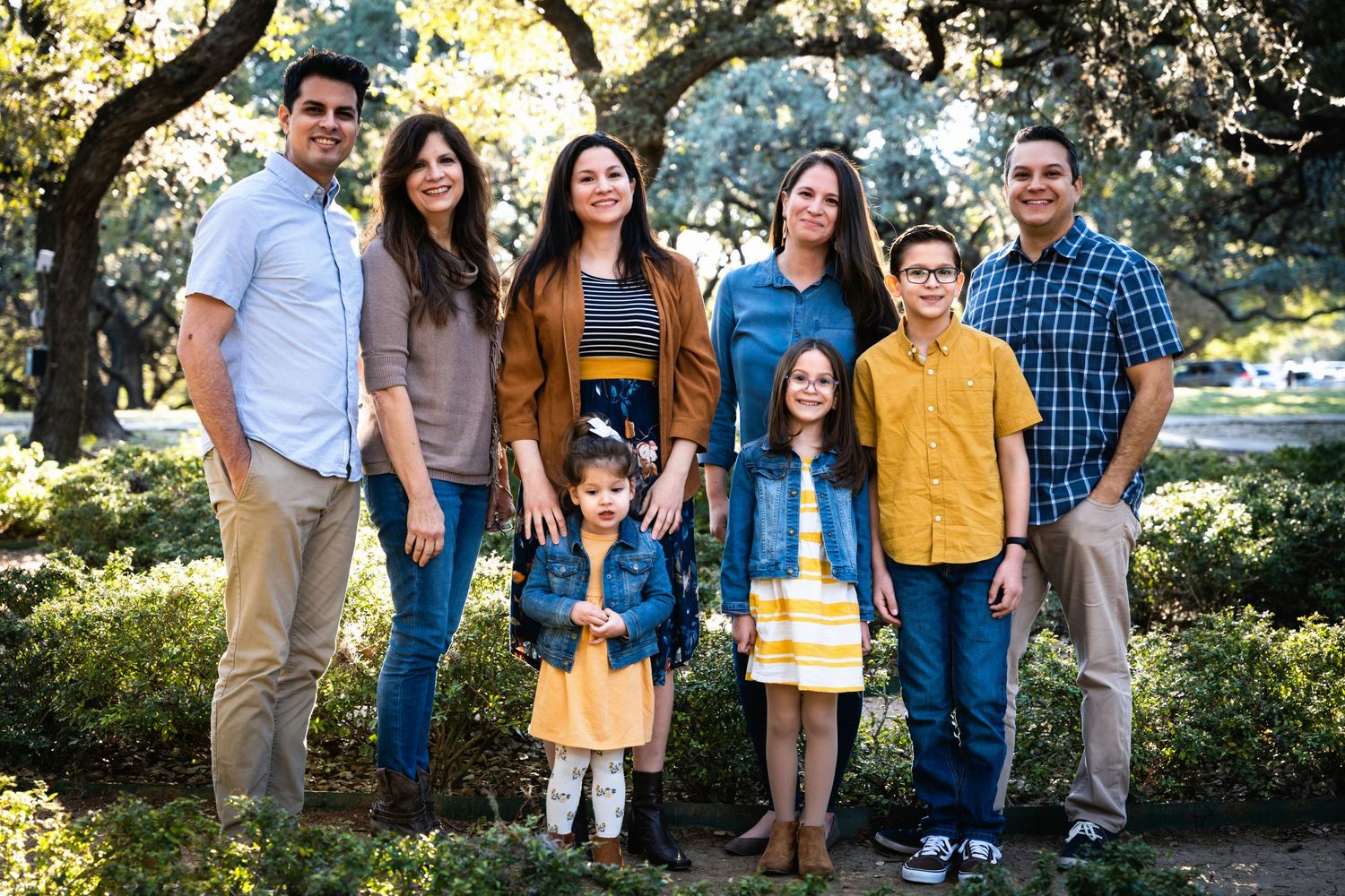 Group outdoor portrait of family members in coordinated casual attire among trees.