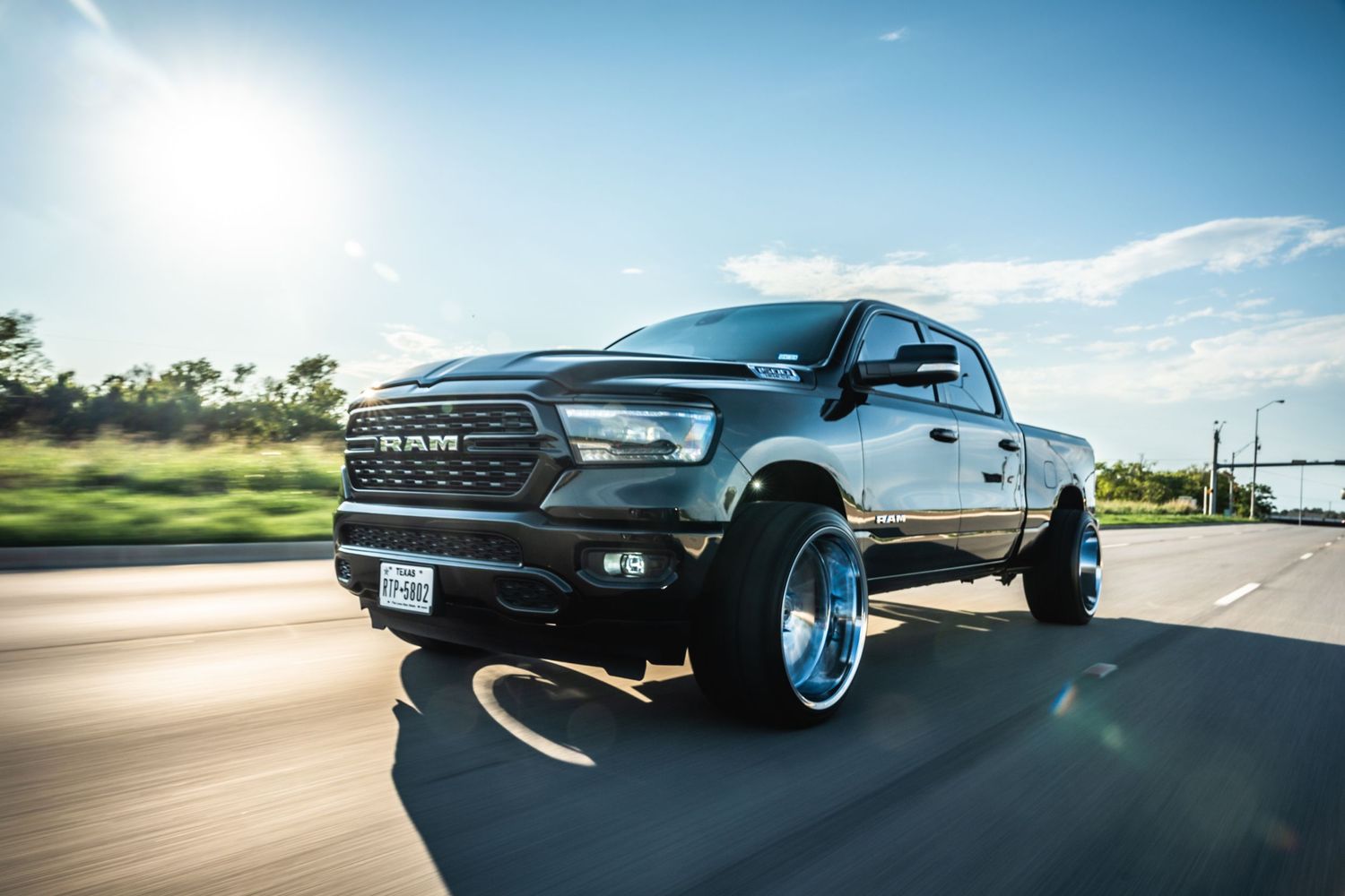 Lifted black RAM truck with aftermarket wheels captured in sunlit action shot.