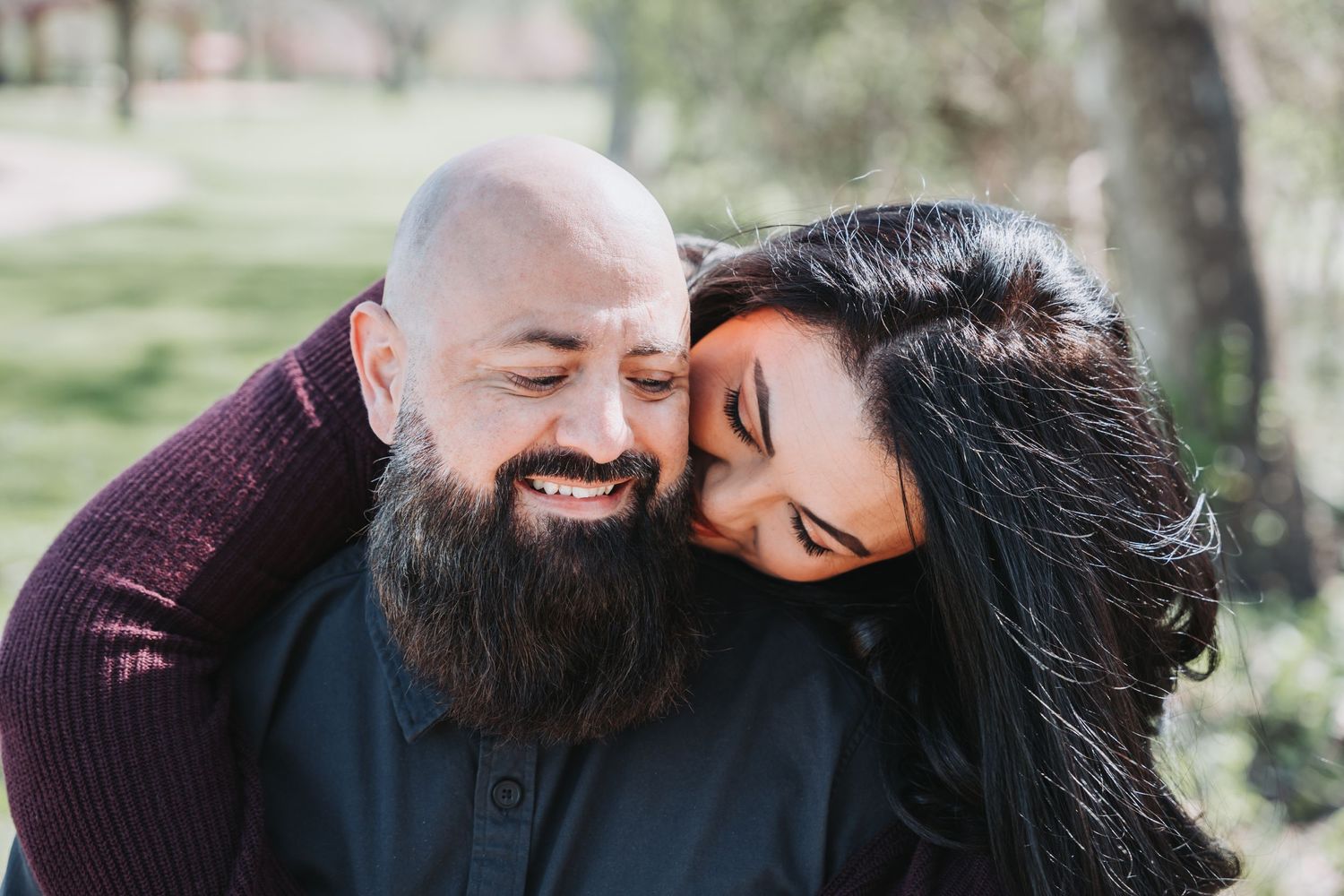 Intimate moment between couple wearing burgundy and black clothing outdoors.