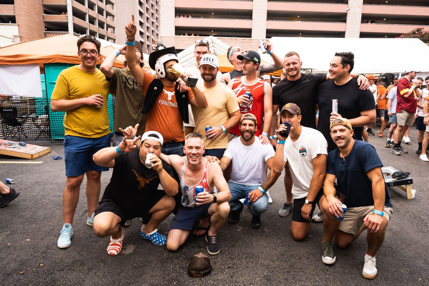 Friends celebrate and pose together at an outdoor tailgate party near a parking structure.