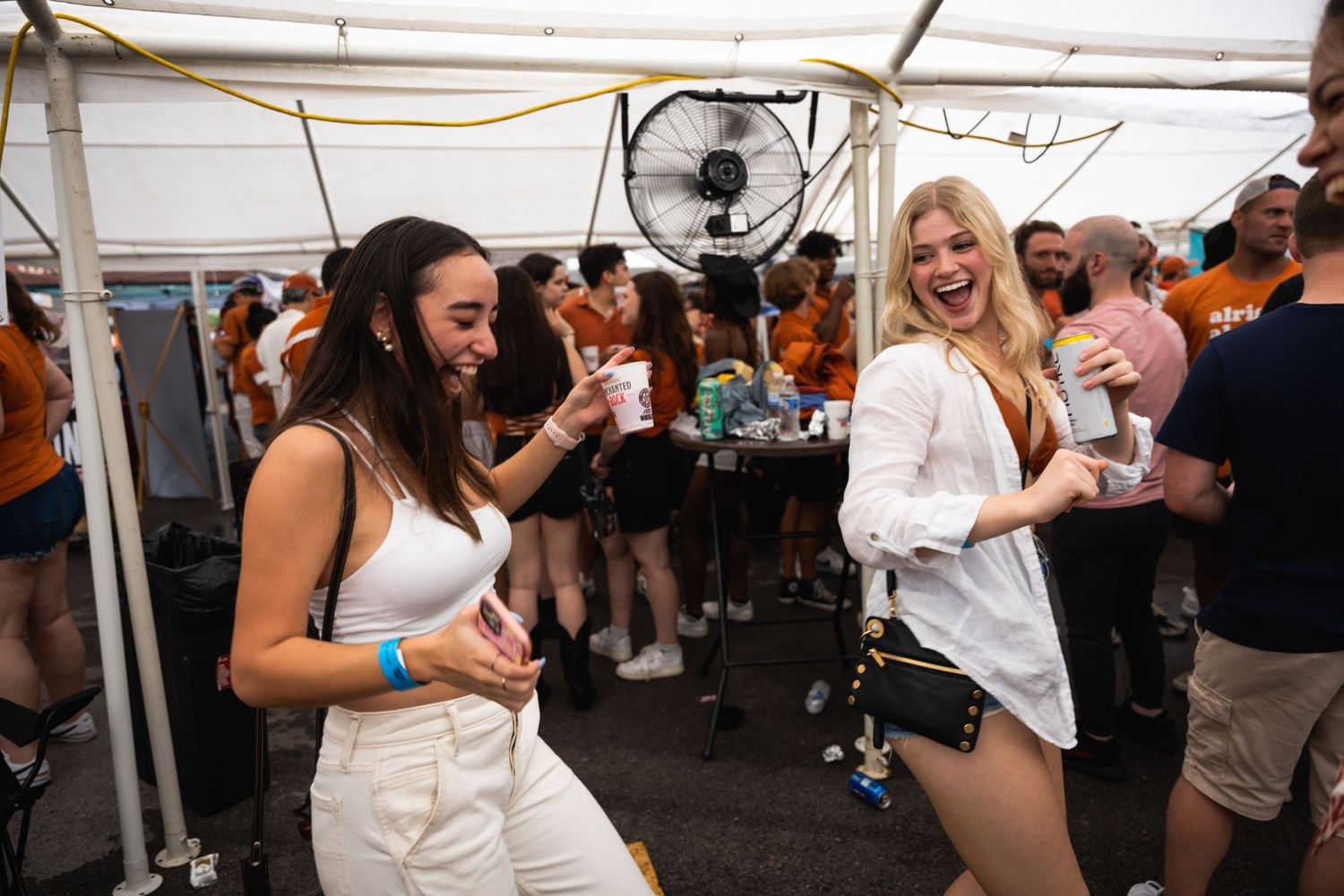 Dancing party goers enjoy themselves under a white tent at an outdoor festival event.