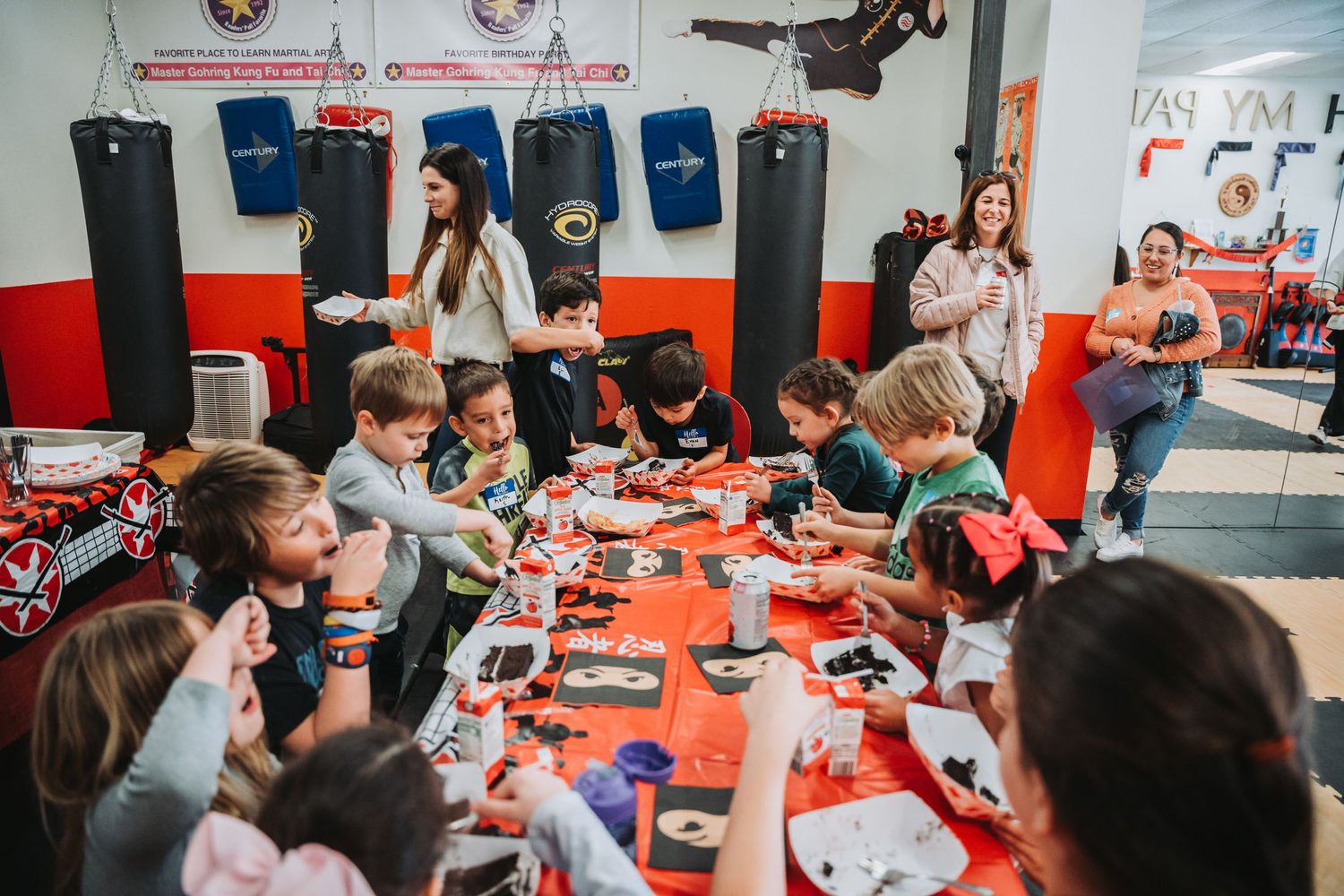 Group of students enjoying party snacks at long table in martial arts studio.