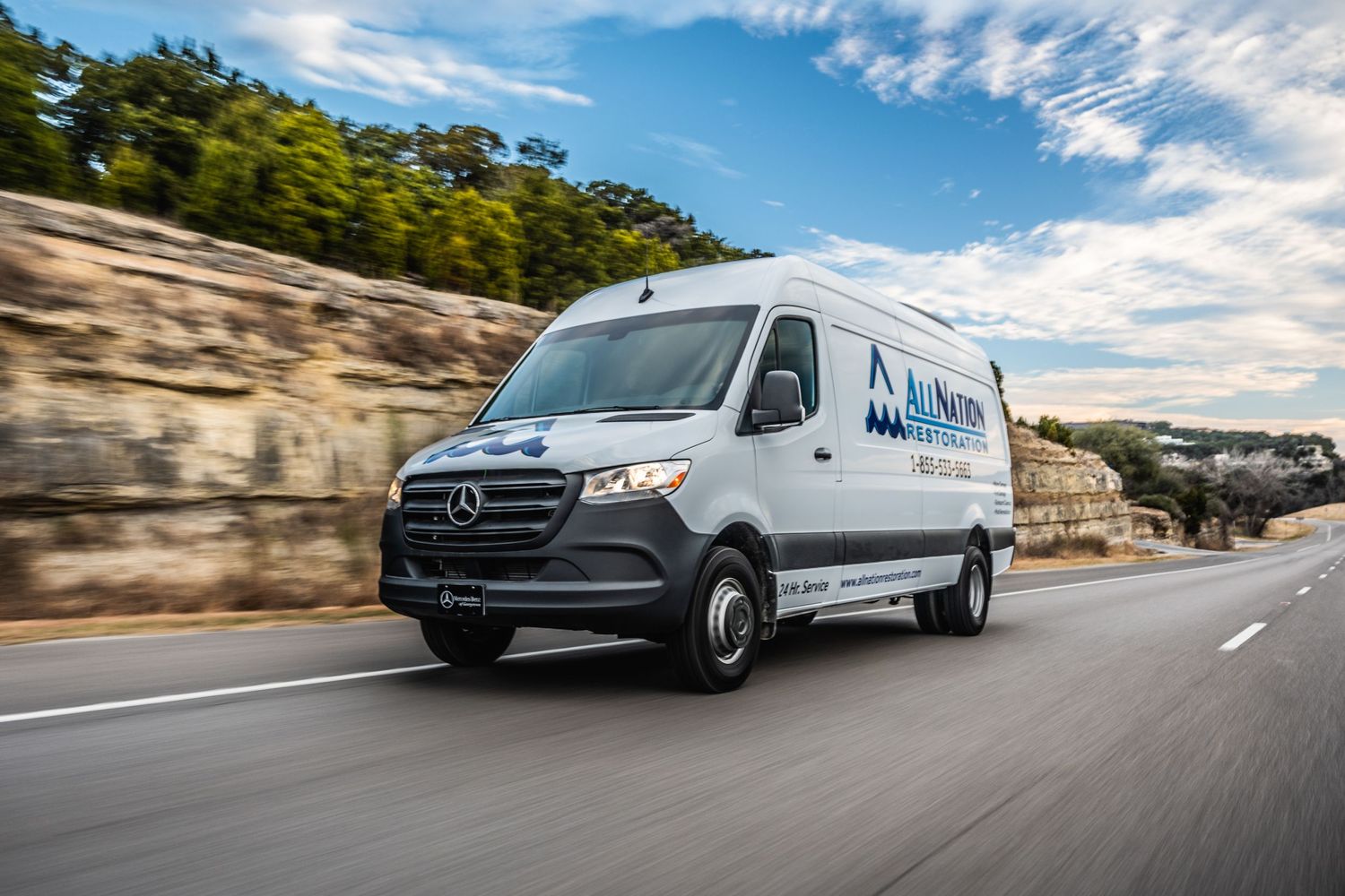 White Mercedes Sprinter delivery van driving on mountain road under blue sky.