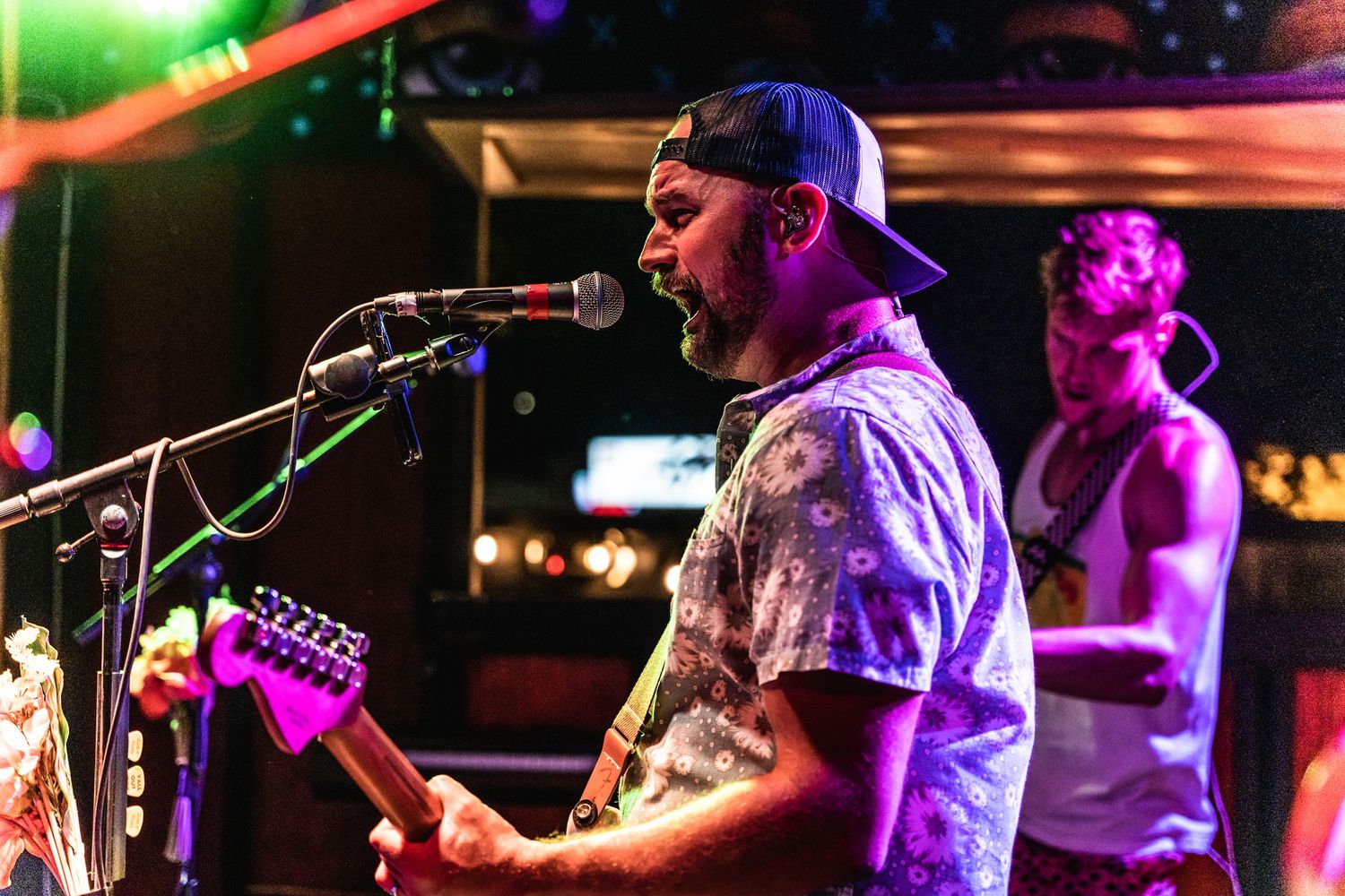 Musician performing with a guitar under colorful stage lighting at a nightclub venue.