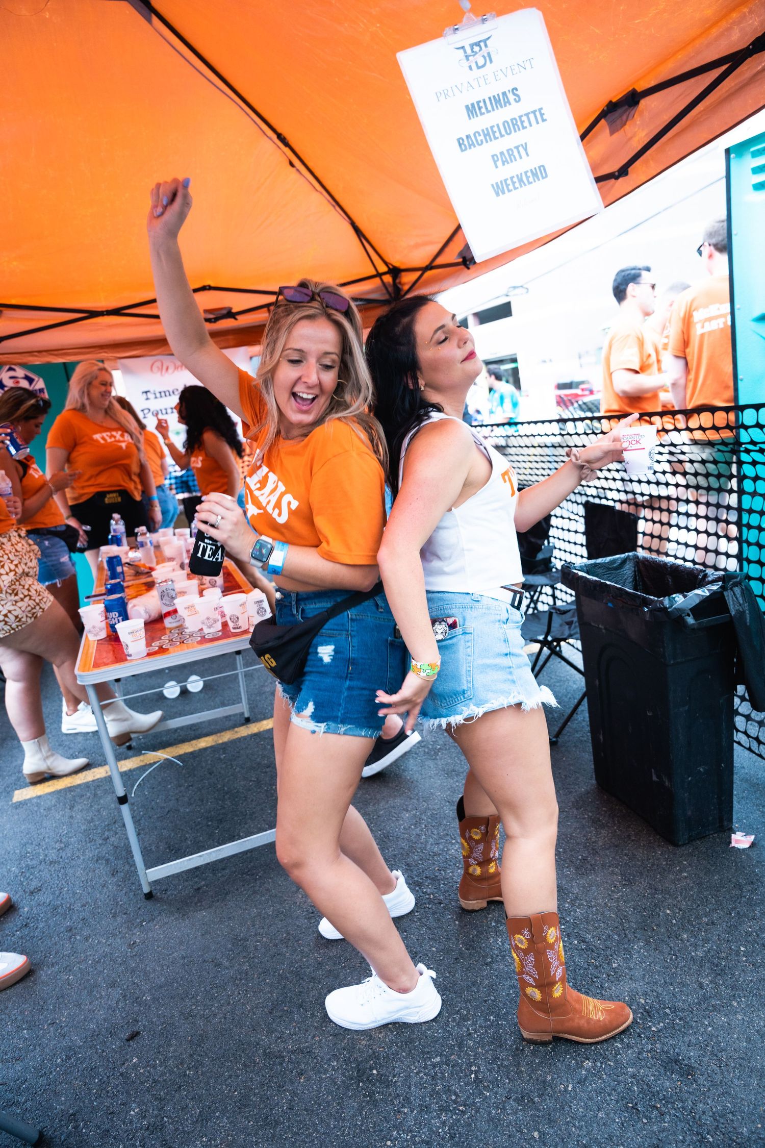 Friends in Texas gear dancing and celebrating at outdoor party under orange tent.