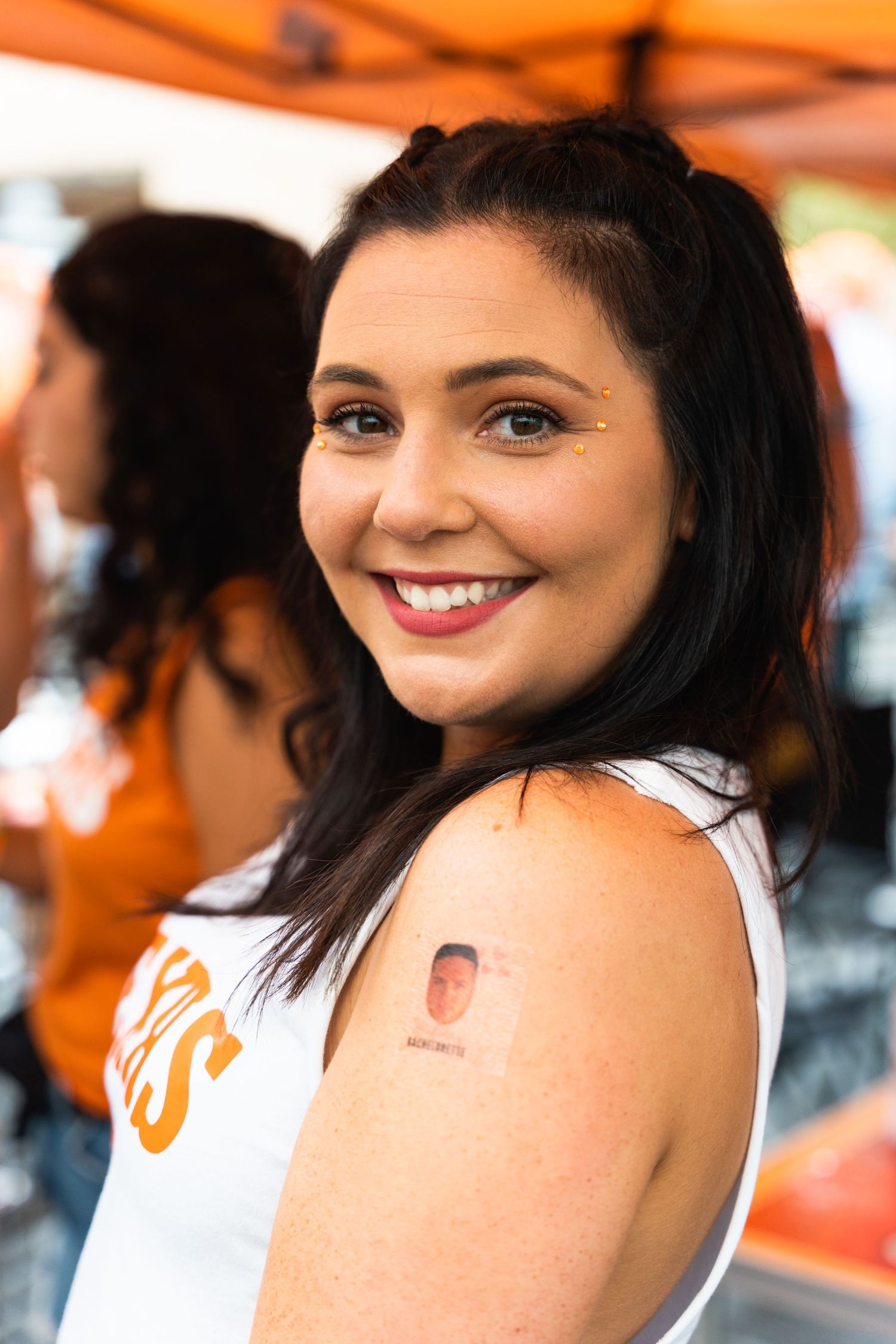 Woman in white tank top smiling at outdoor party with orange decorations.