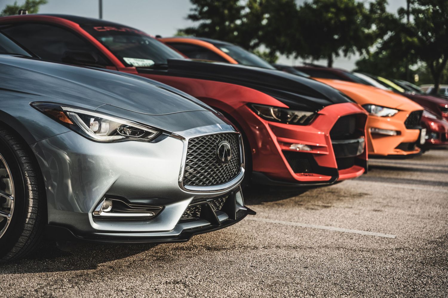Three luxury sports cars lined up showing their front grilles and headlights in silver, red and orange colors.