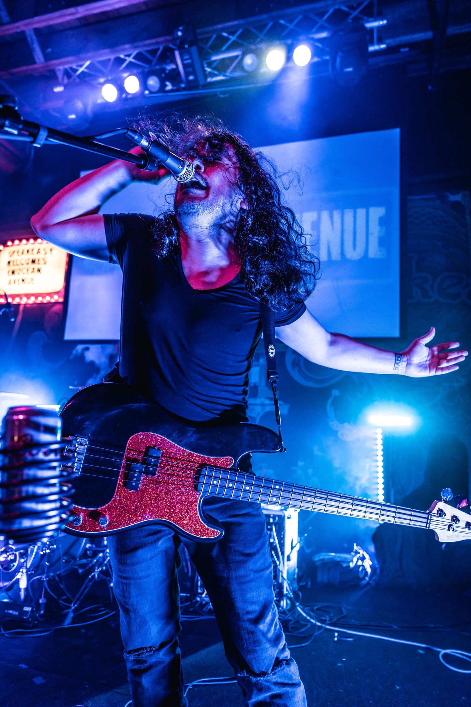 Bassist with red guitar performs energetically under blue stage lights.