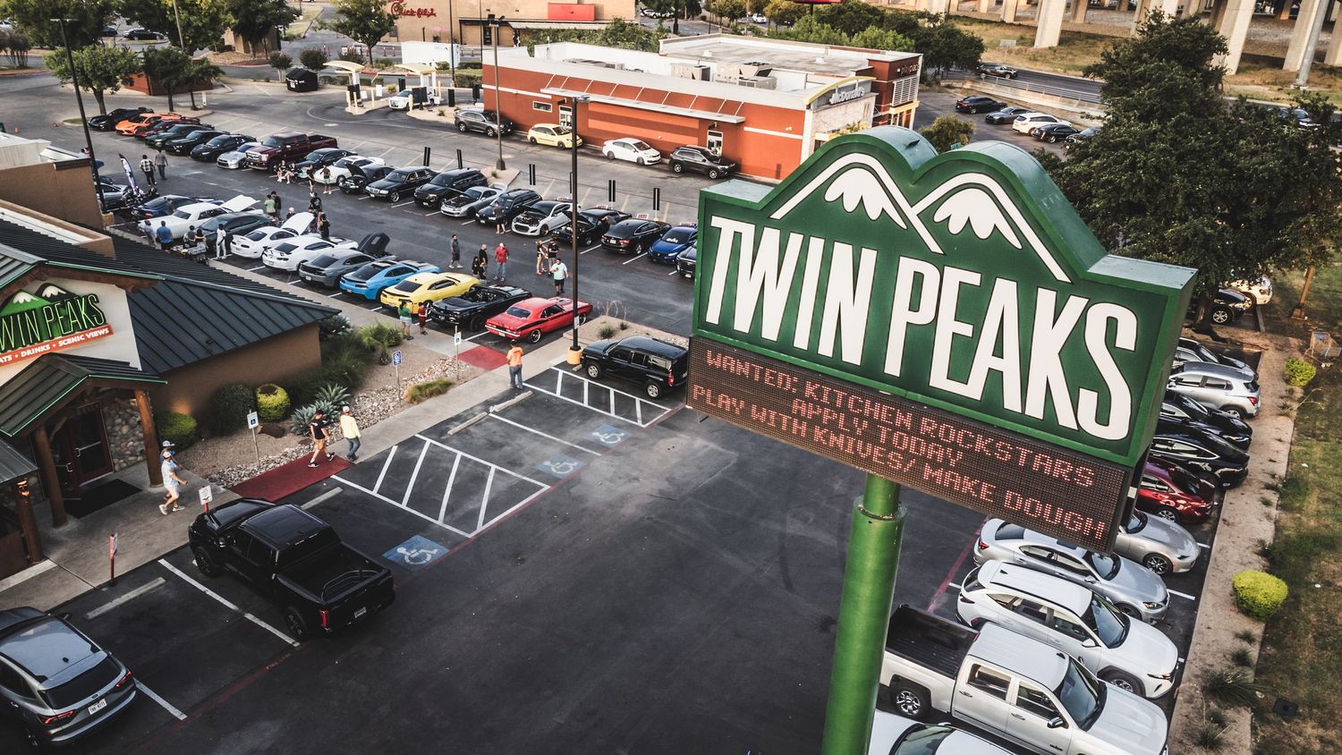 Twin Peaks restaurant sign and parking lot filled with cars during an auto show event.