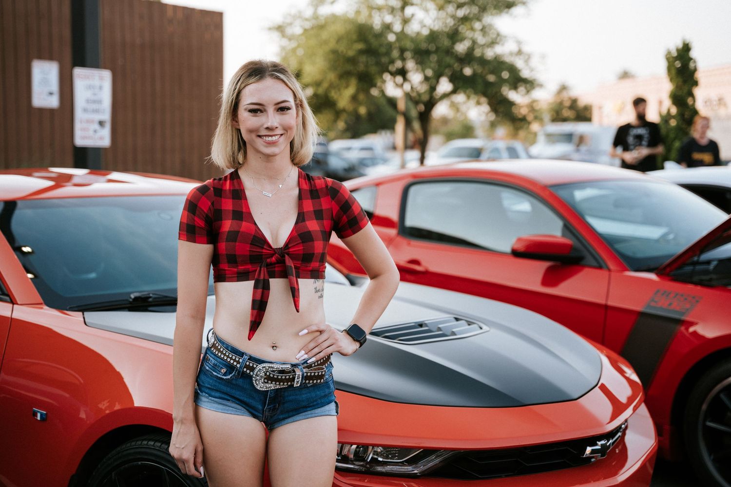 A red Chevrolet Camaro with custom hood and modifications displayed at an outdoor car show.