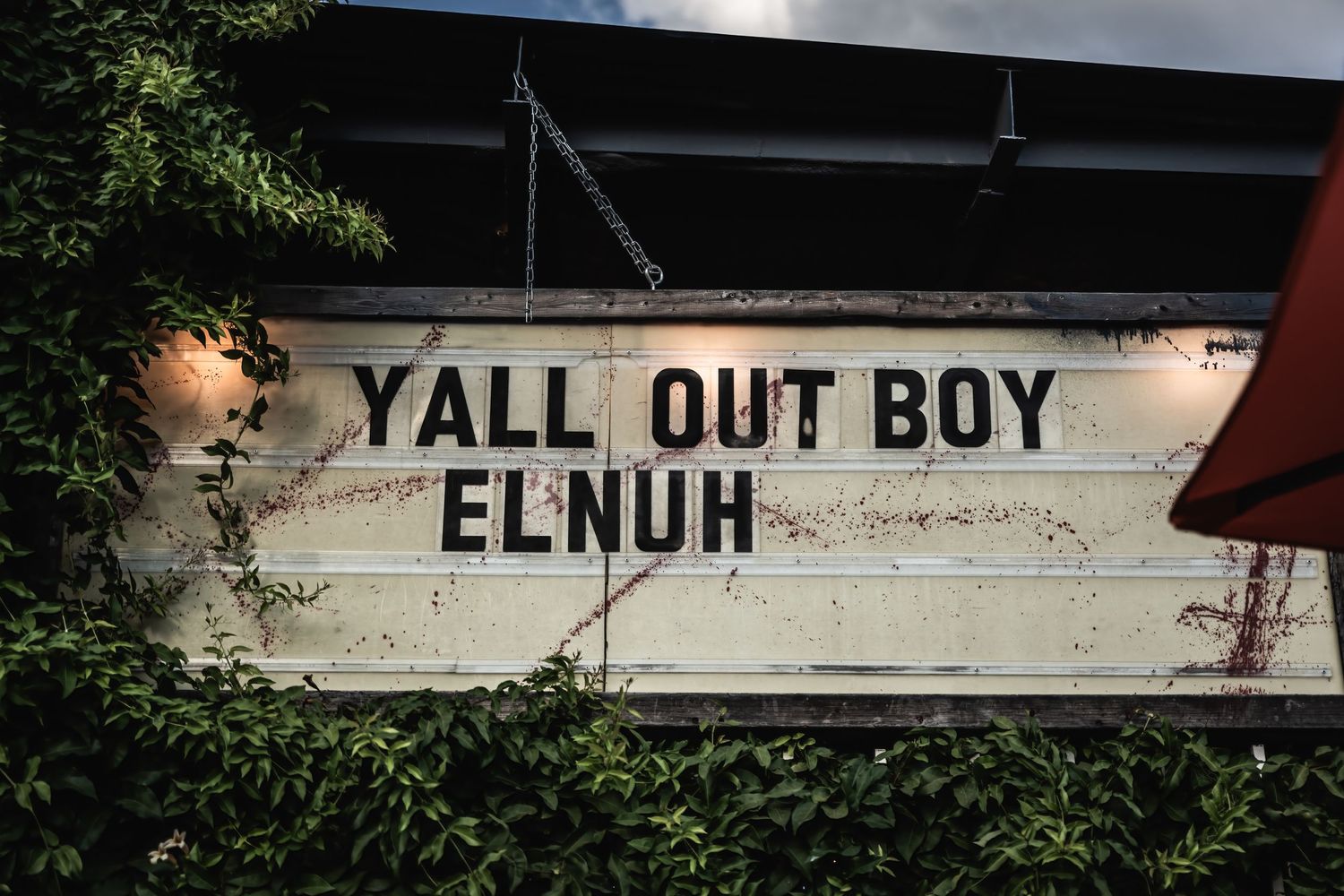 A weathered sign on a wall reads 'YALL OUT BOY ELNUH' in black text.
