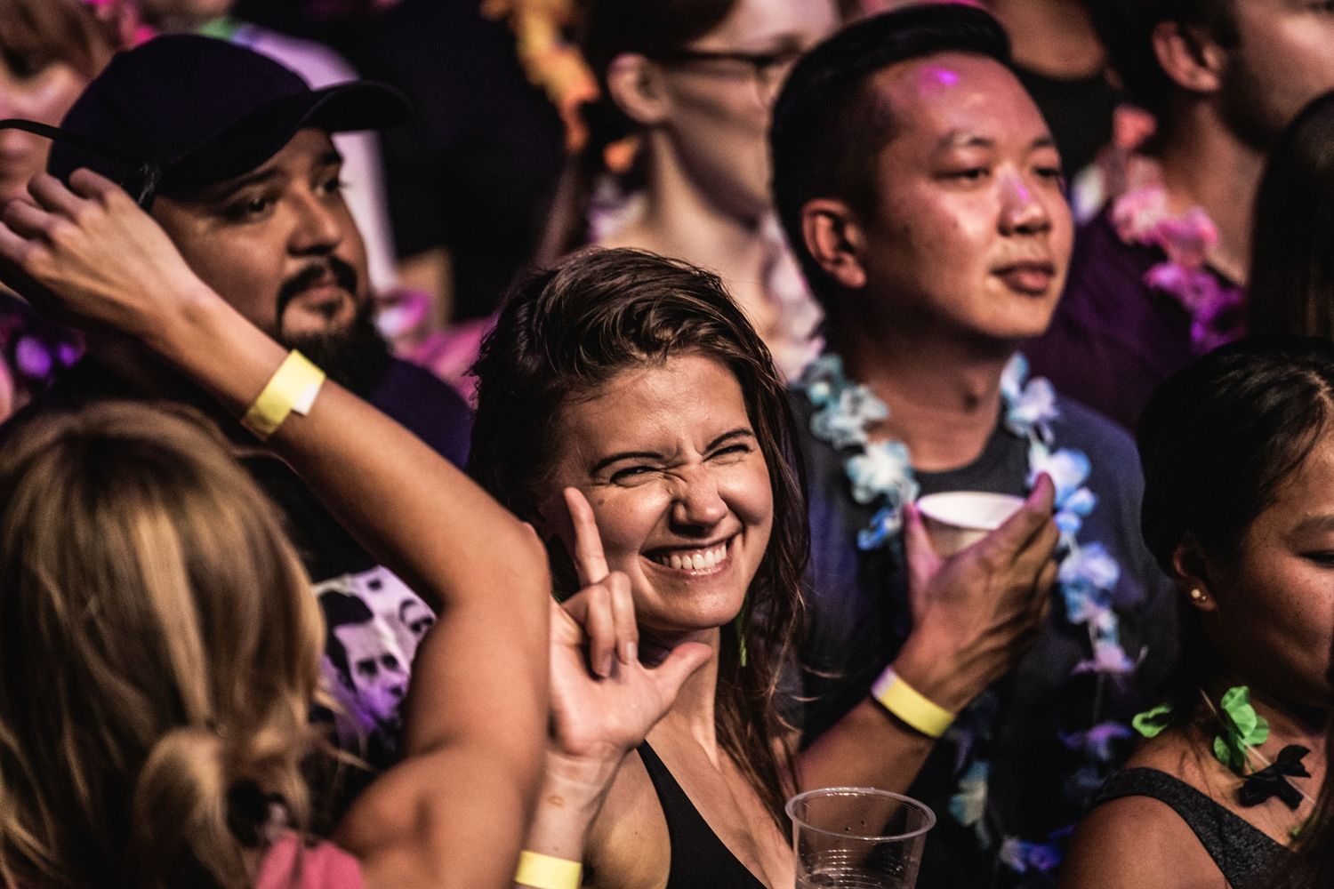 Concert crowd enjoying the show with enthusiastic expressions and raised hands in purple lighting.