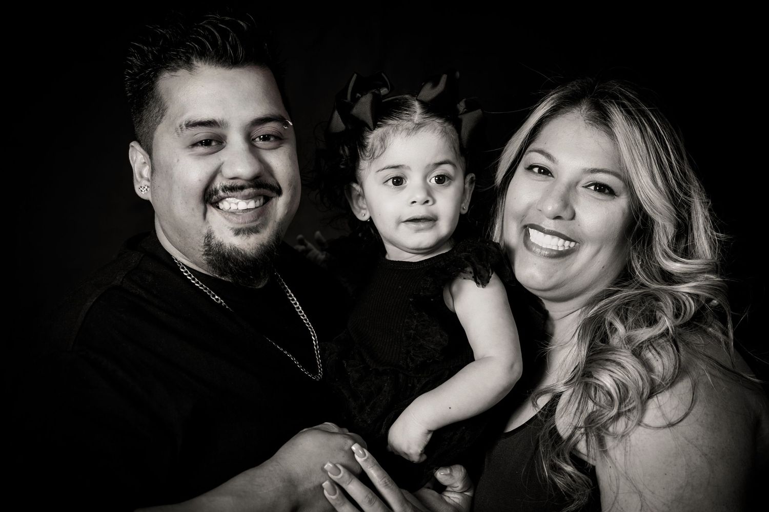 Artistic black and white family portrait showing joyful expressions against dark backdrop.