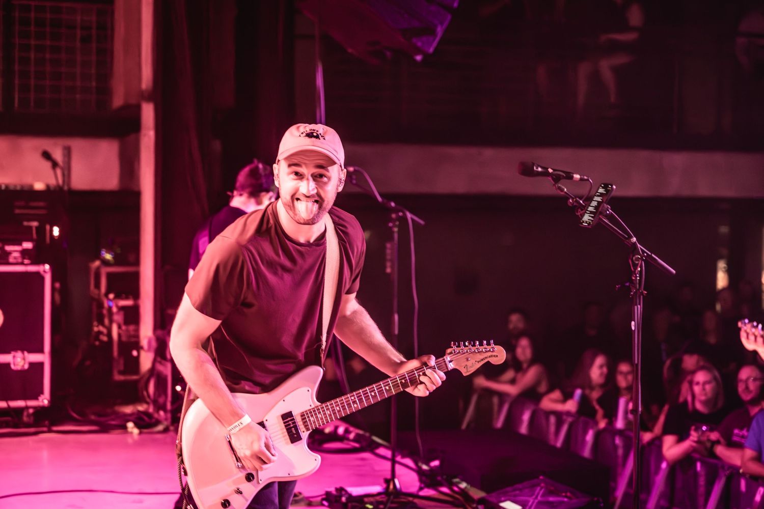 Musician playing electric guitar under red stage lighting during live performance.