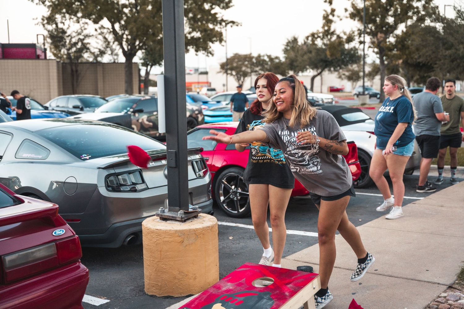 People playing cornhole game in parking lot at outdoor gathering.