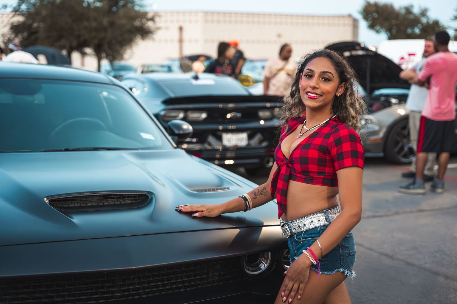 Modern sports car meet featuring a red plaid top and denim shorts style against a teal muscle car.
