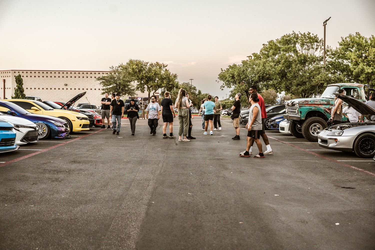 Car enthusiasts gathering at a sunset meetup with modified vehicles on display.