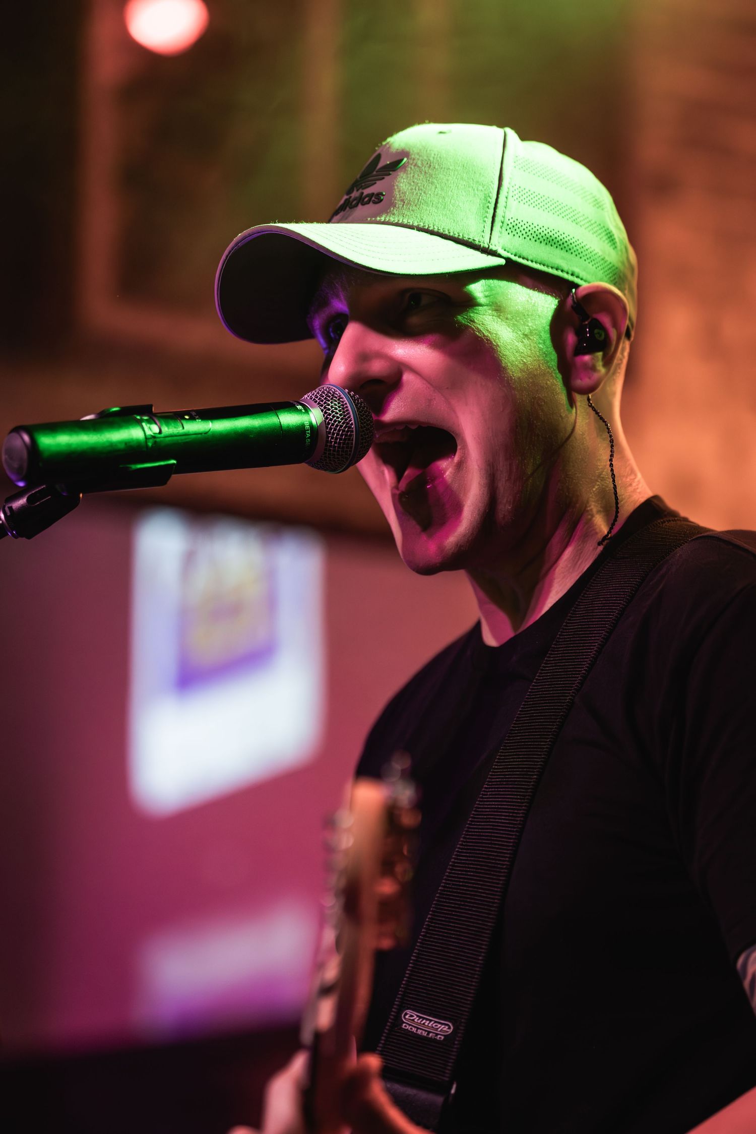 Singer in baseball cap performing with passion under dramatic colored stage lighting.