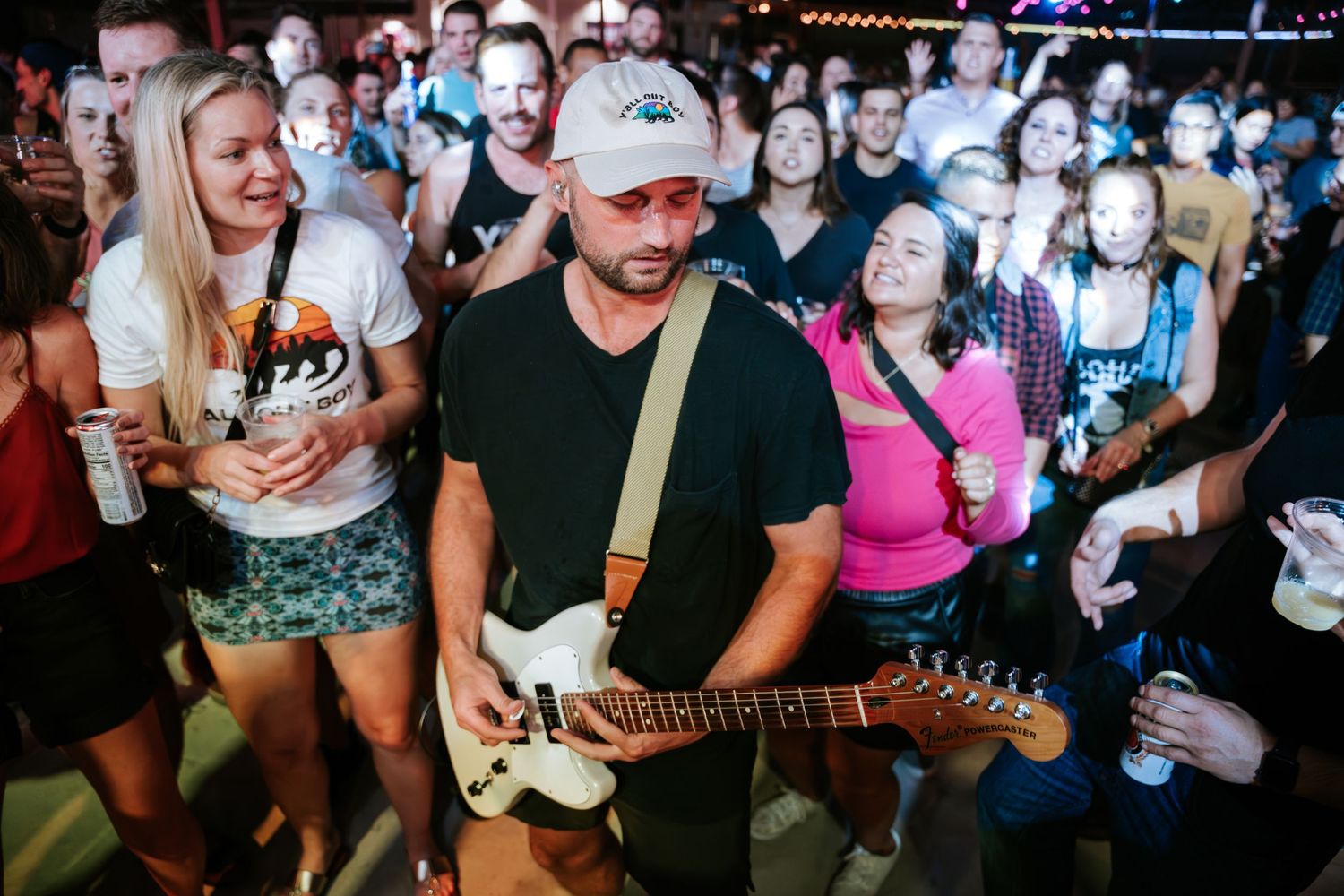 Musician plays electric guitar while surrounded by enthusiastic fans at an indoor concert venue.