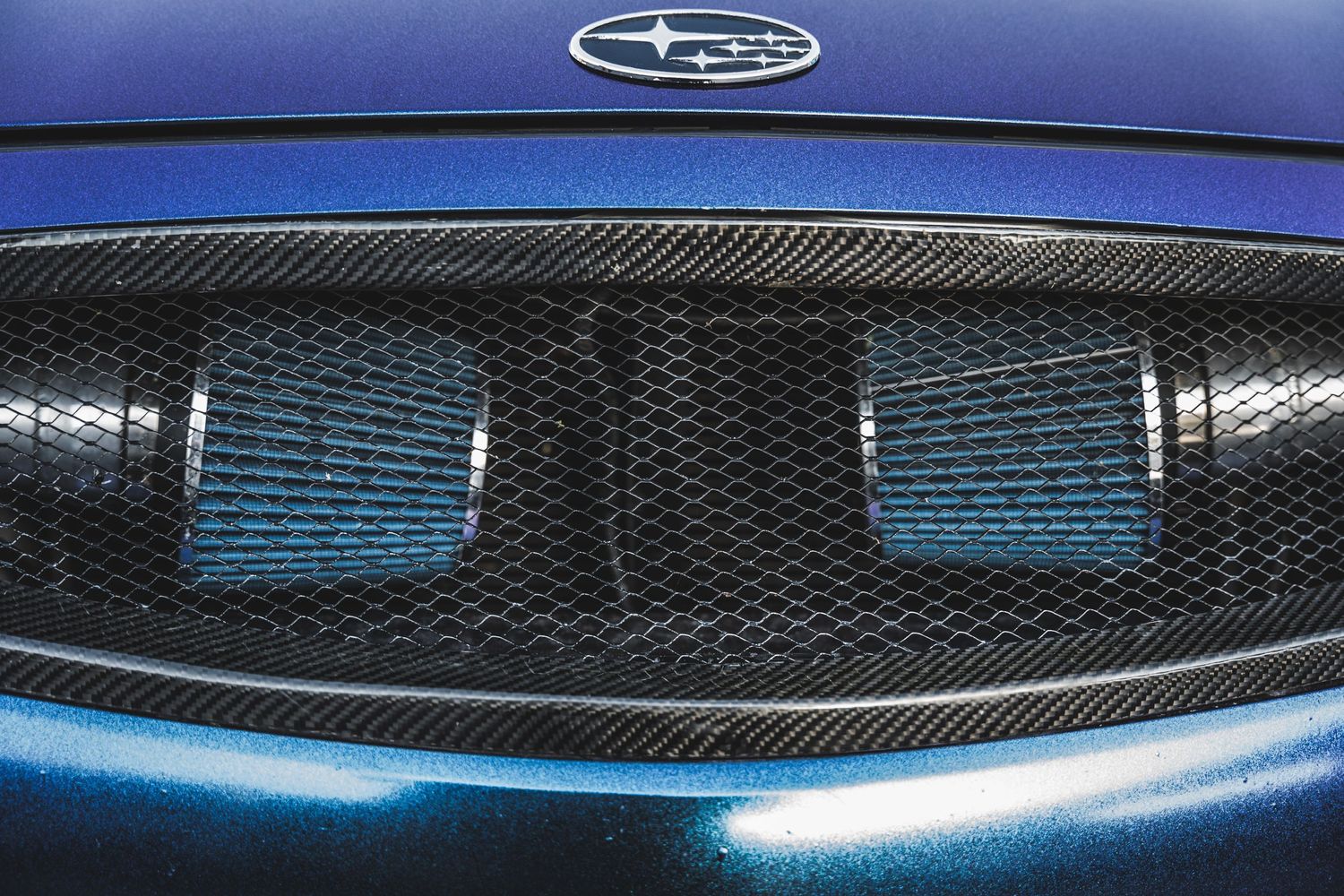 Close-up of a Subaru hood scoop with carbon fiber mesh pattern and blue accents.