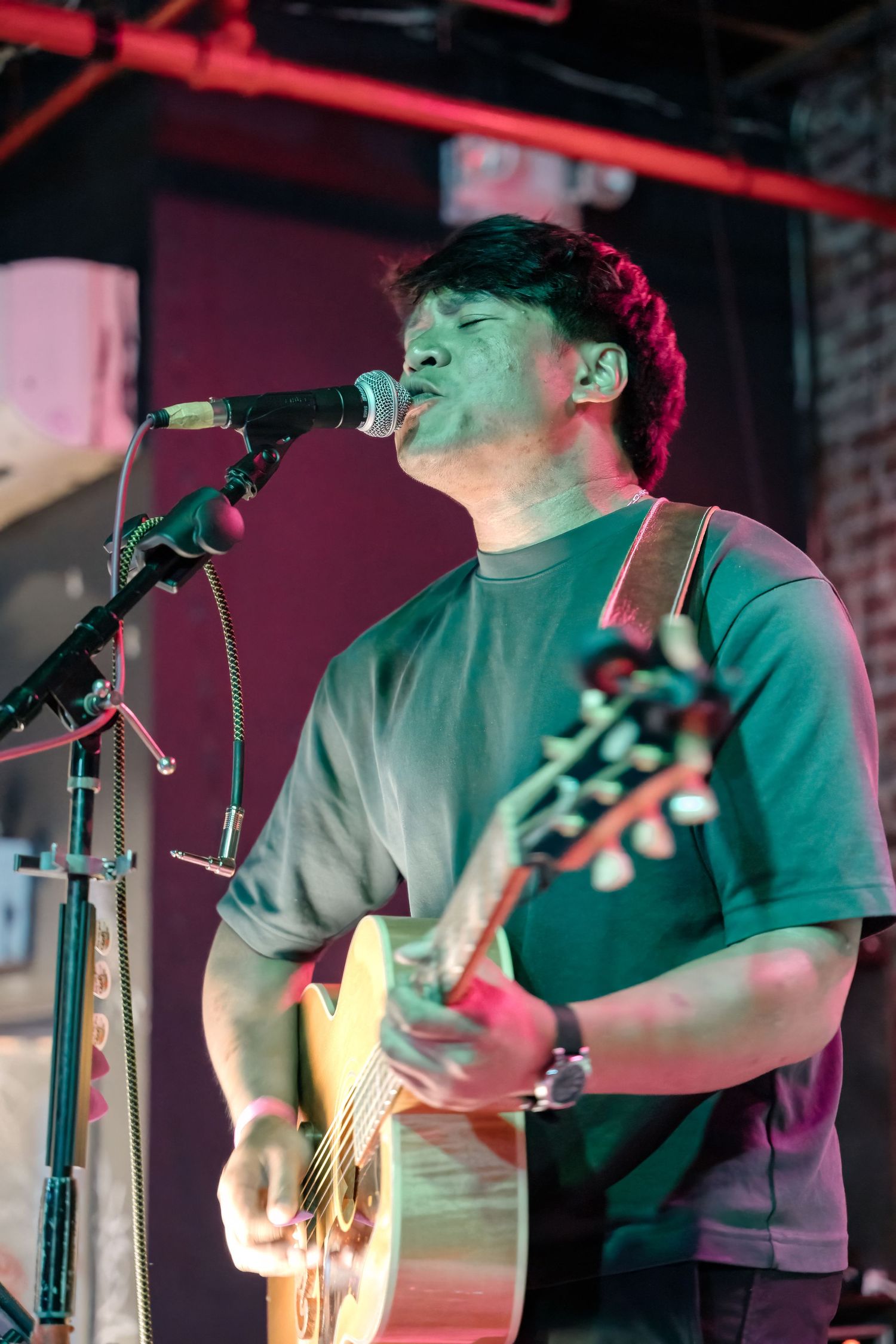 Musician performing on stage with acoustic guitar under red lighting.