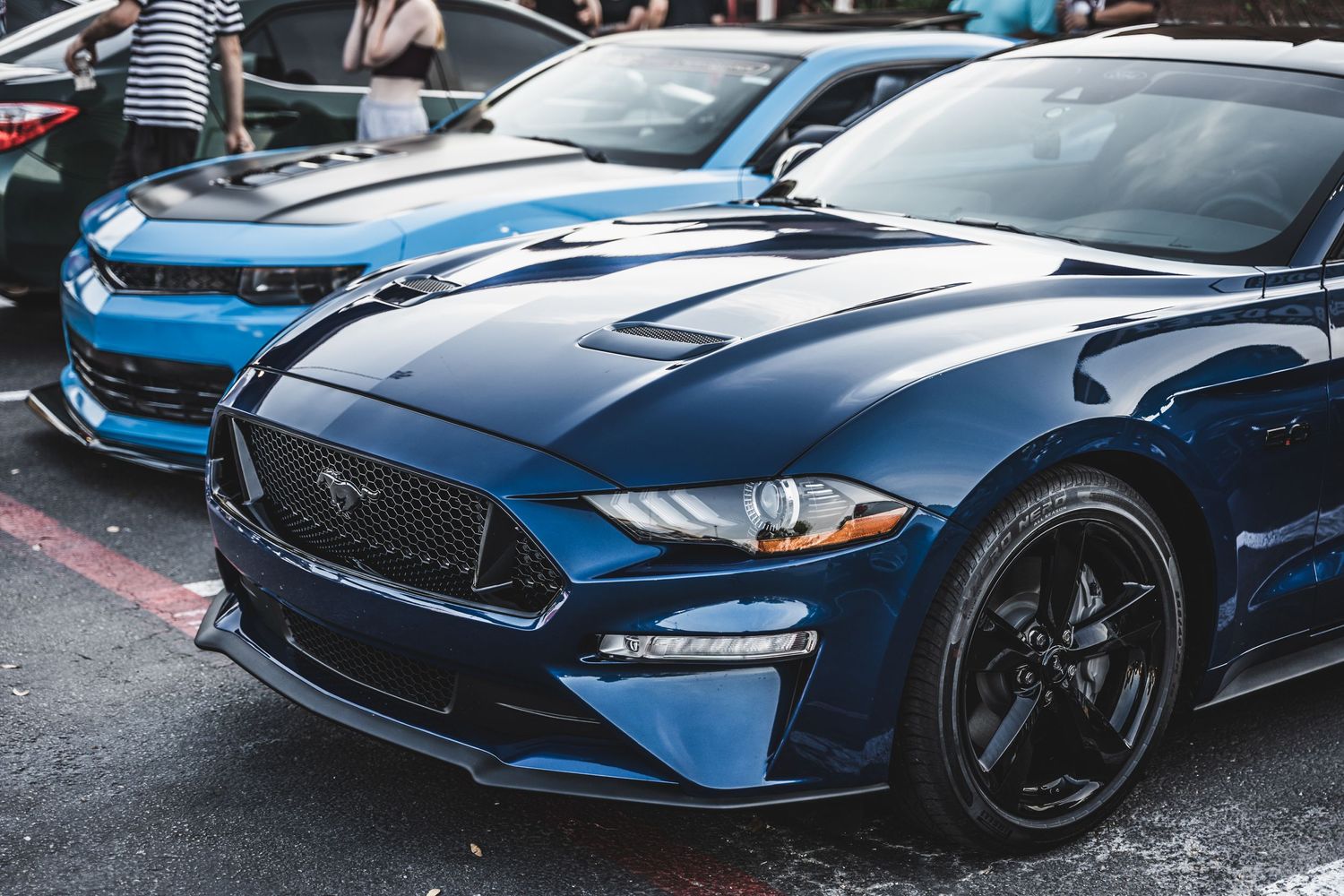 Close-up view of a blue Ford Mustang front end with black wheels at a car show.