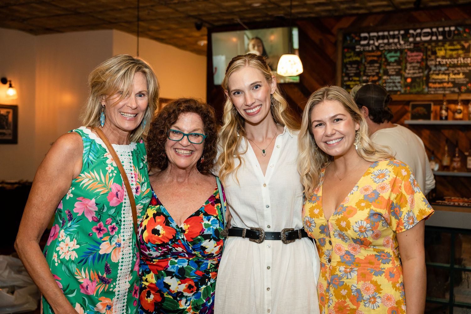Four friends in colorful summer attire gather at a casual restaurant.