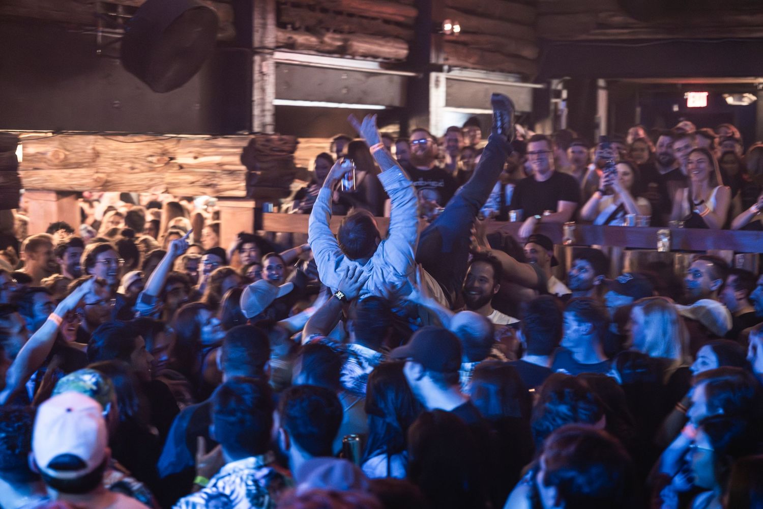Concert crowd surfing during a high-energy performance with blue stage lighting.