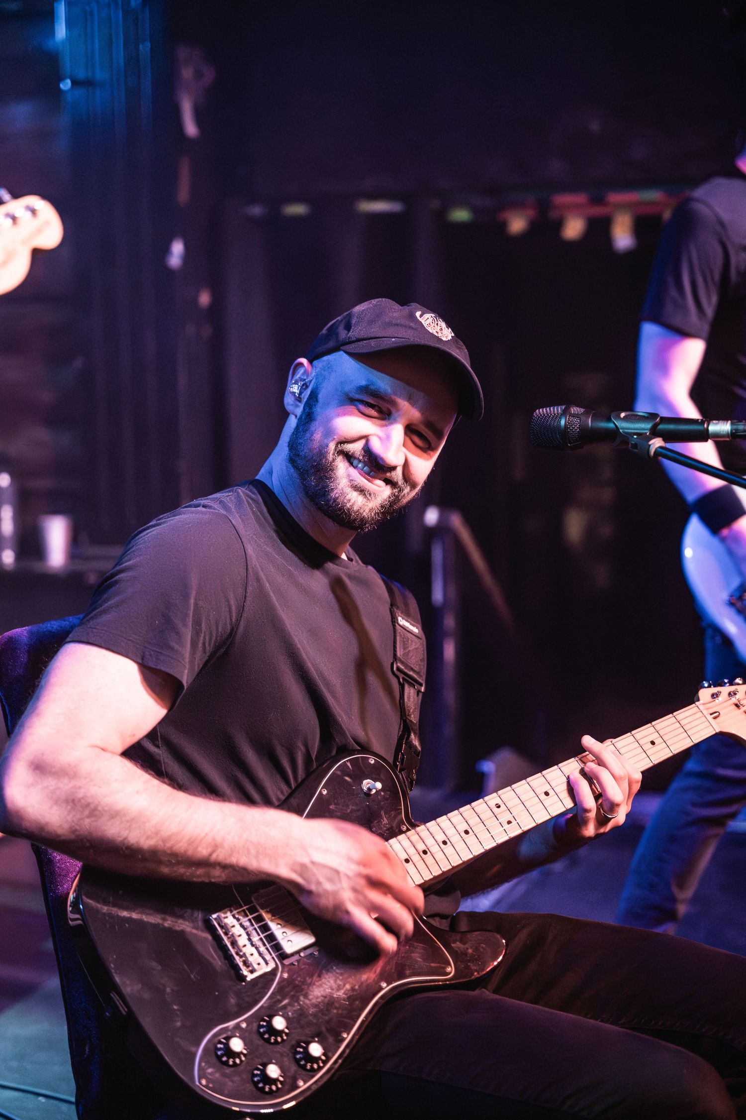 A musician plays an electric guitar on stage during a performance with blue lighting effects.