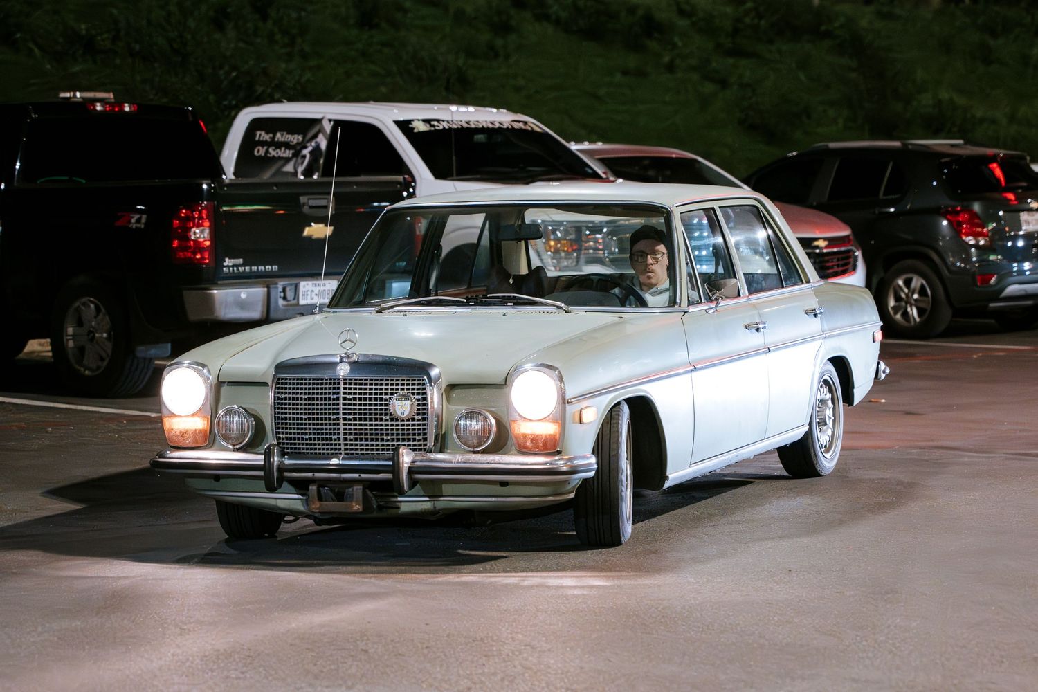 Classic white Mercedes-Benz sedan with vintage styling parked under nighttime lighting.