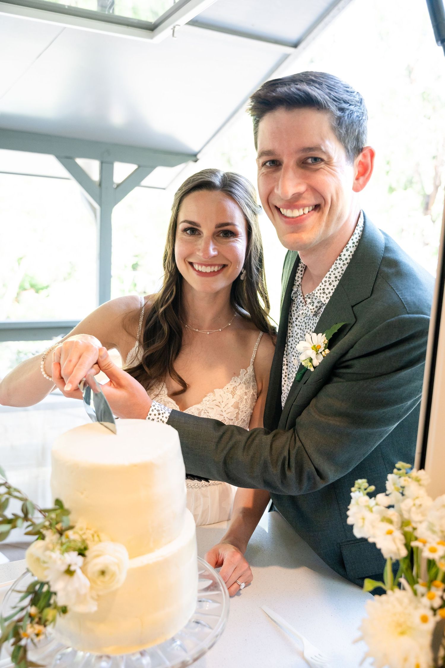 Happy couple cutting their elegant white wedding cake together under covered pavilion.