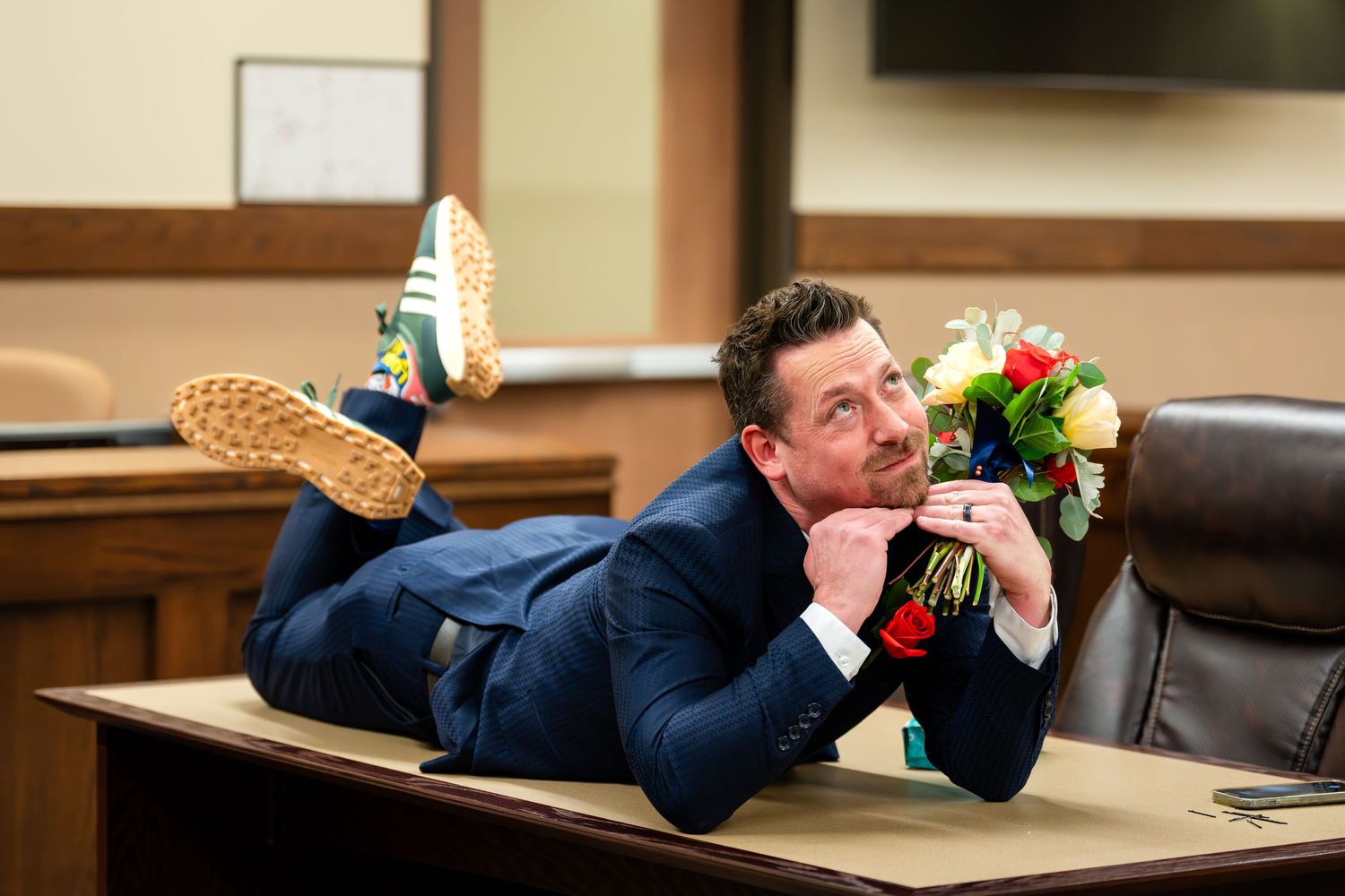 Person lounges on courthouse desk holding flowers with feet up in a playful pose.