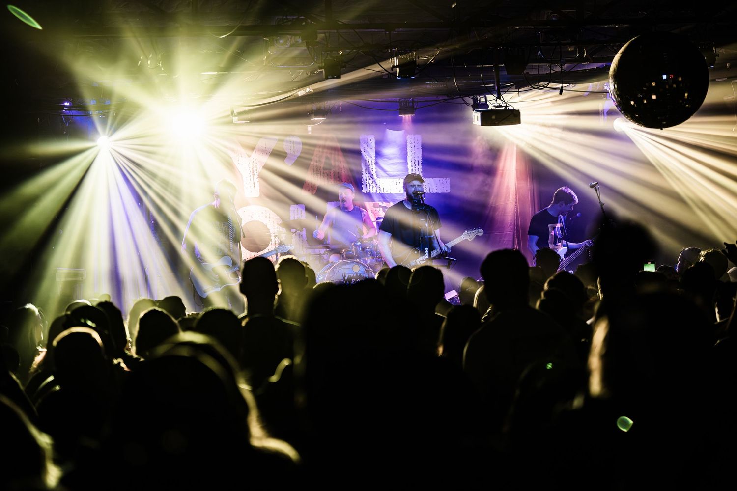 Concert crowd silhouettes with dramatic yellow and purple stage lighting effects.