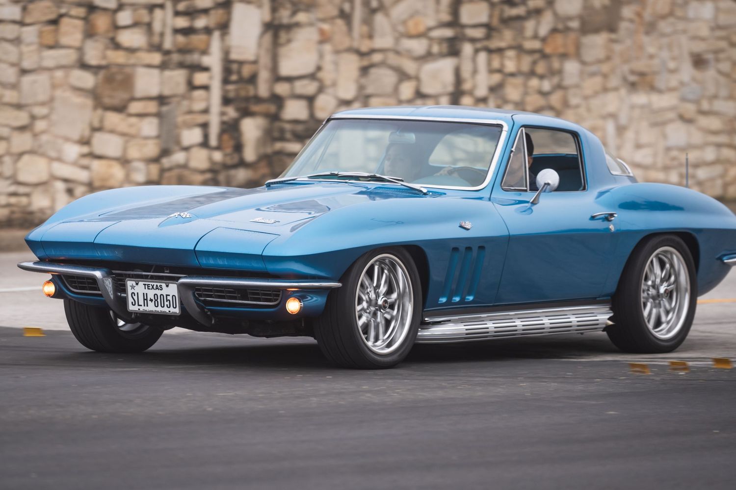 Classic blue Chevrolet Corvette Stingray photographed against a stone wall background.